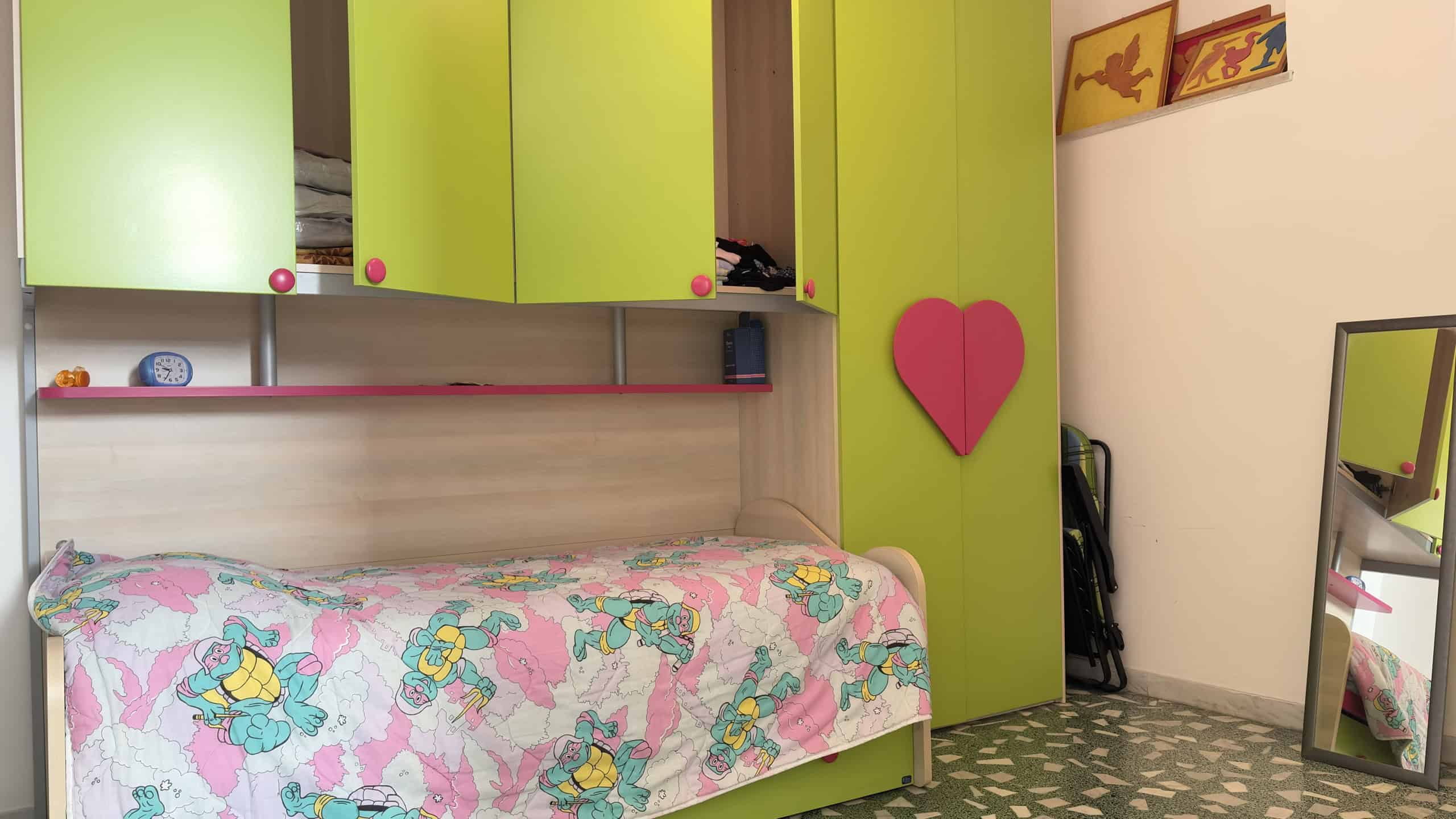 Letto singolo con armadio a ponte verde lime e dettagli rosa, in una camera da letto moderna e colorata. Ideale per ambienti giovani e vivaci, con spazio di archiviazione funzionale e decorazioni alle.