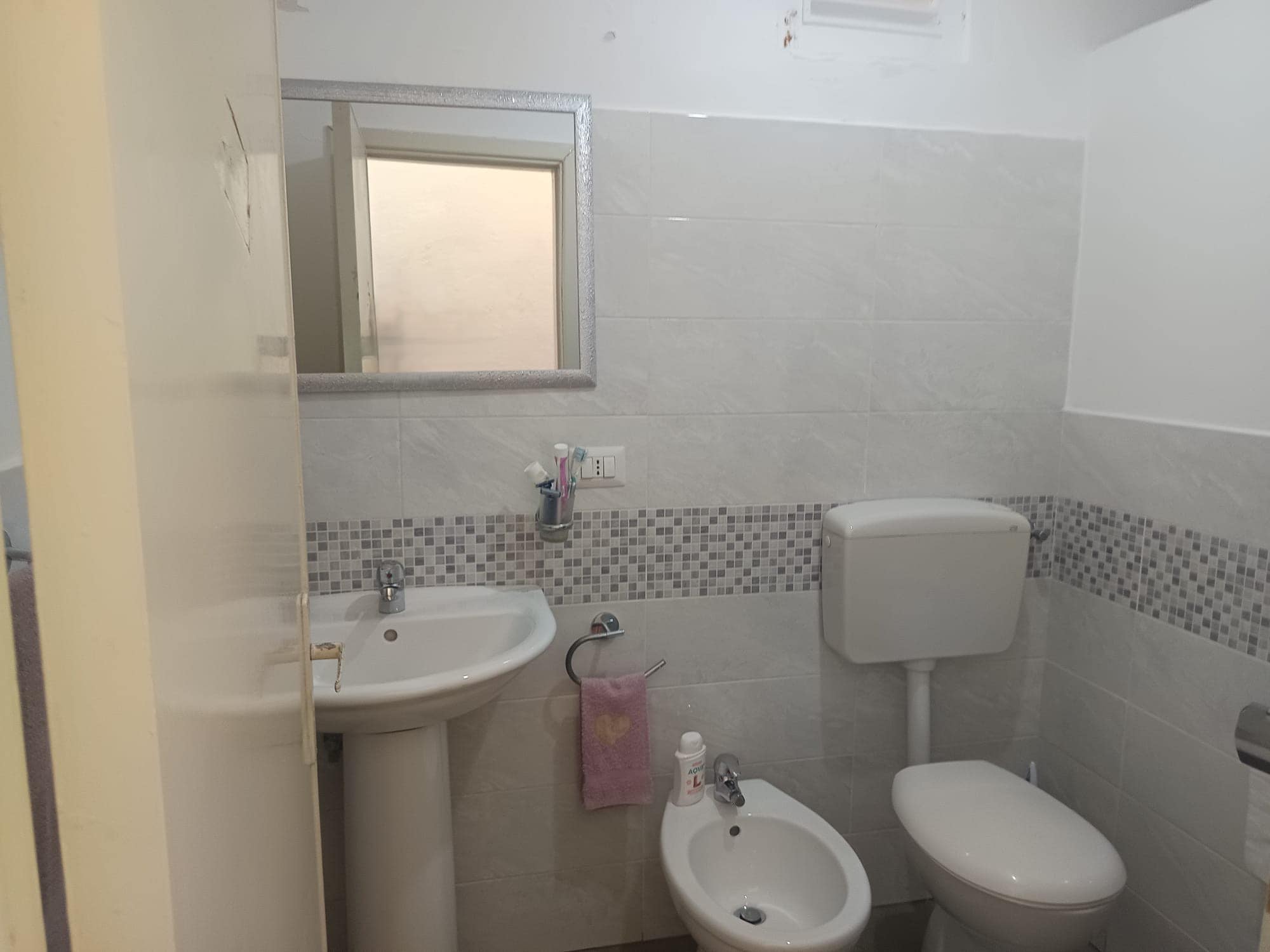 Lavabo e WC in un bagno moderno con piastrelle chiare e dettagli decorativi in mosaico, ambiente pulito e funzionale.