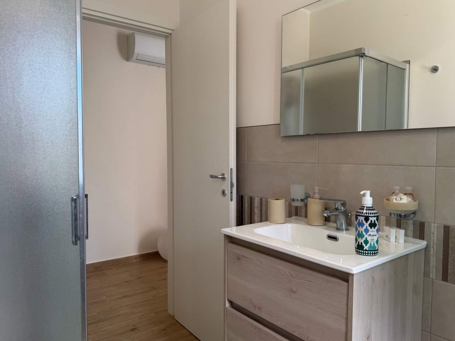 Lavabo moderno in bagno con mobili in legno chiaro, specchio grande e accessori eleganti, ambiente luminoso e funzionale.