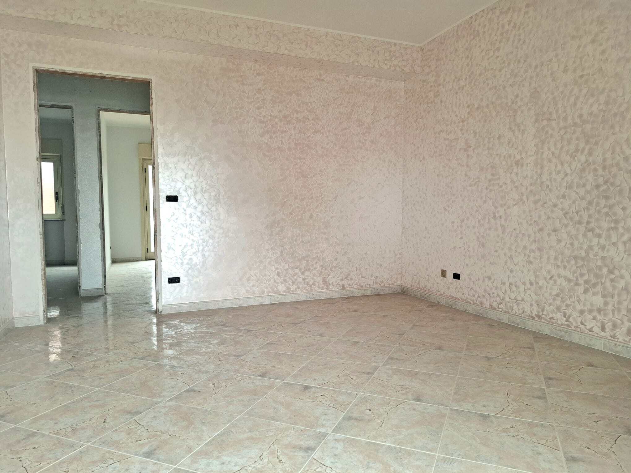 Appartamento vuoto con pareti color pesca e pavimento in piastrelle beige, spazio luminoso e spazioso, pronto per essere arredato e personalizzato. Ideale per famiglie o investitori immobiliari.