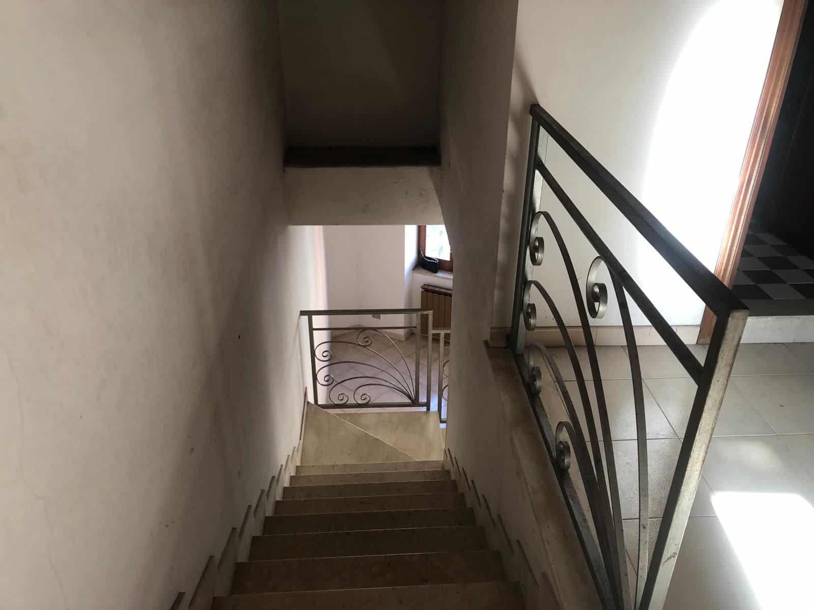 Scale di una scala interna in un edificio residenziale, con ringhiera in ferro battuto e pareti bianche, illuminata dalla luce naturale proveniente da una finestra.