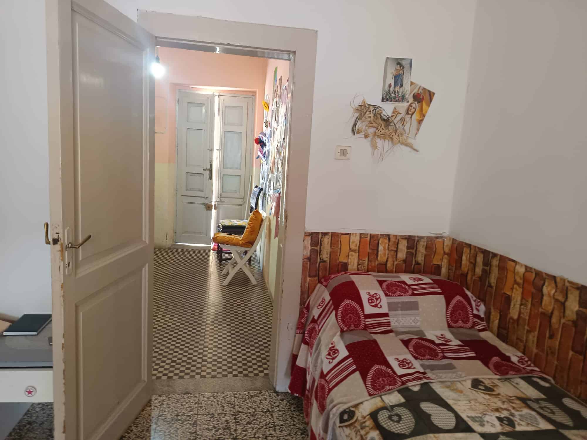 Camera da letto accogliente con pareti bianche, letto con copriletto rosso e decorazioni artistiche, in un ambiente domestico semplice e confortevole.