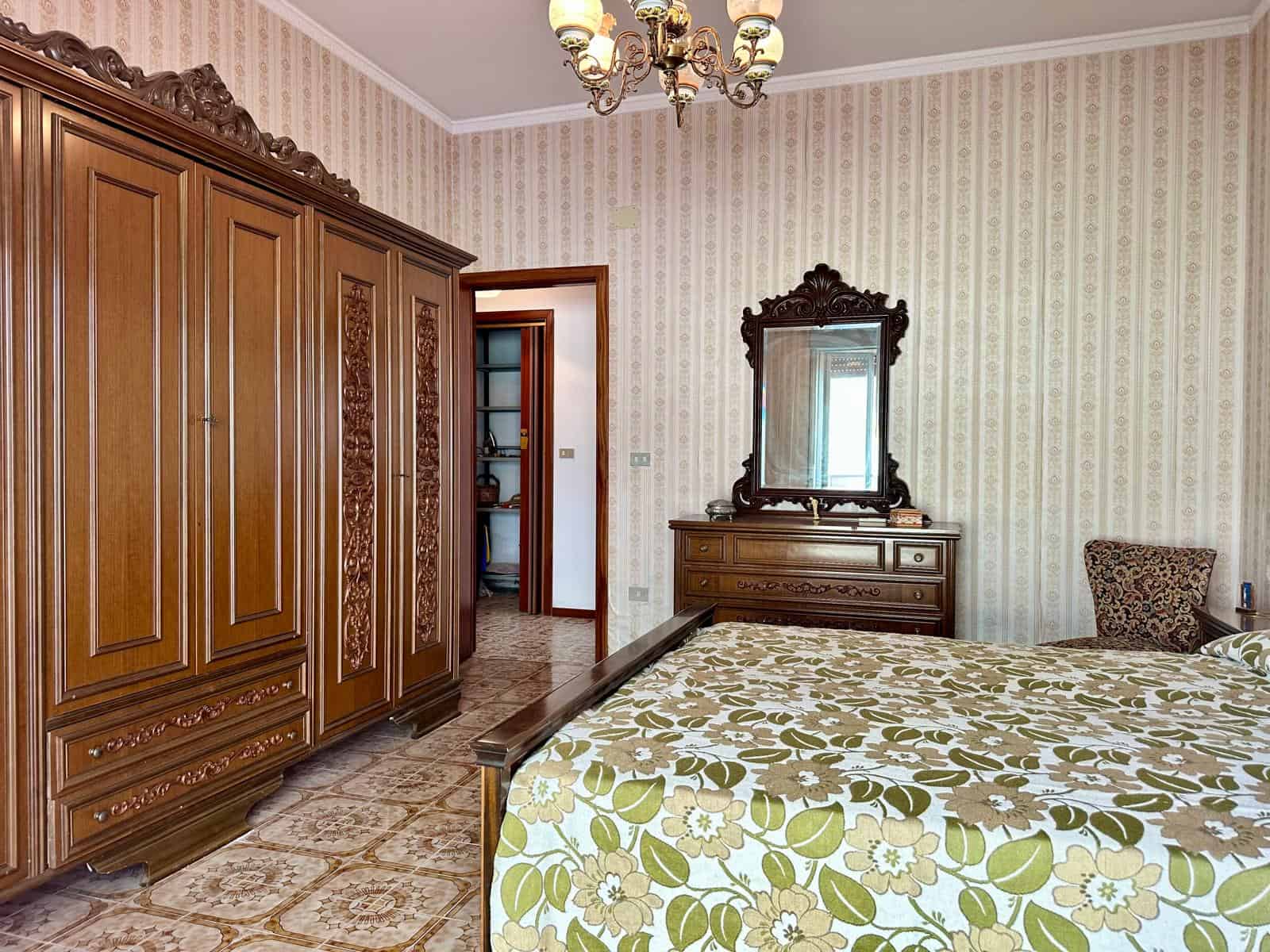 Camera da letto con arredi in stile classico, armadio in legno massiccio e specchio decorato, ambiente luminoso e accogliente.