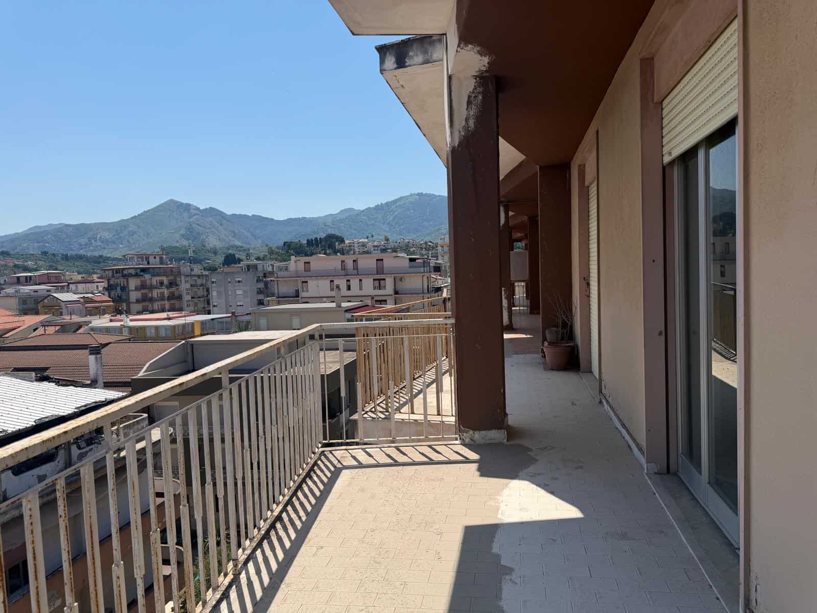 Balcone di un appartamento con vista sulle montagne, con ringhiera in metallo e pavimento in piastrelle, in un contesto urbano residenziale.