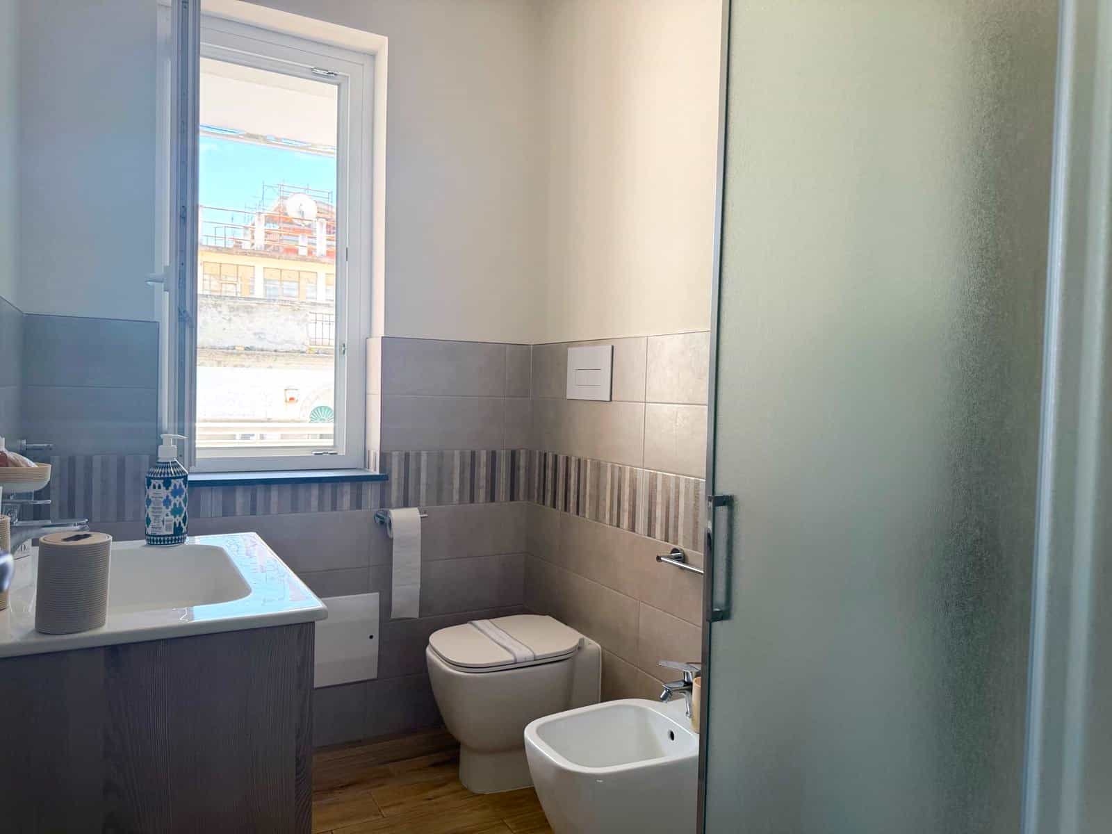 Pannello di bagno moderno con finestra, lavabo, WC e bidet in un ambiente luminoso e rinnovato, ideale per case e appartamenti in vendita o affitto a NextCasa.