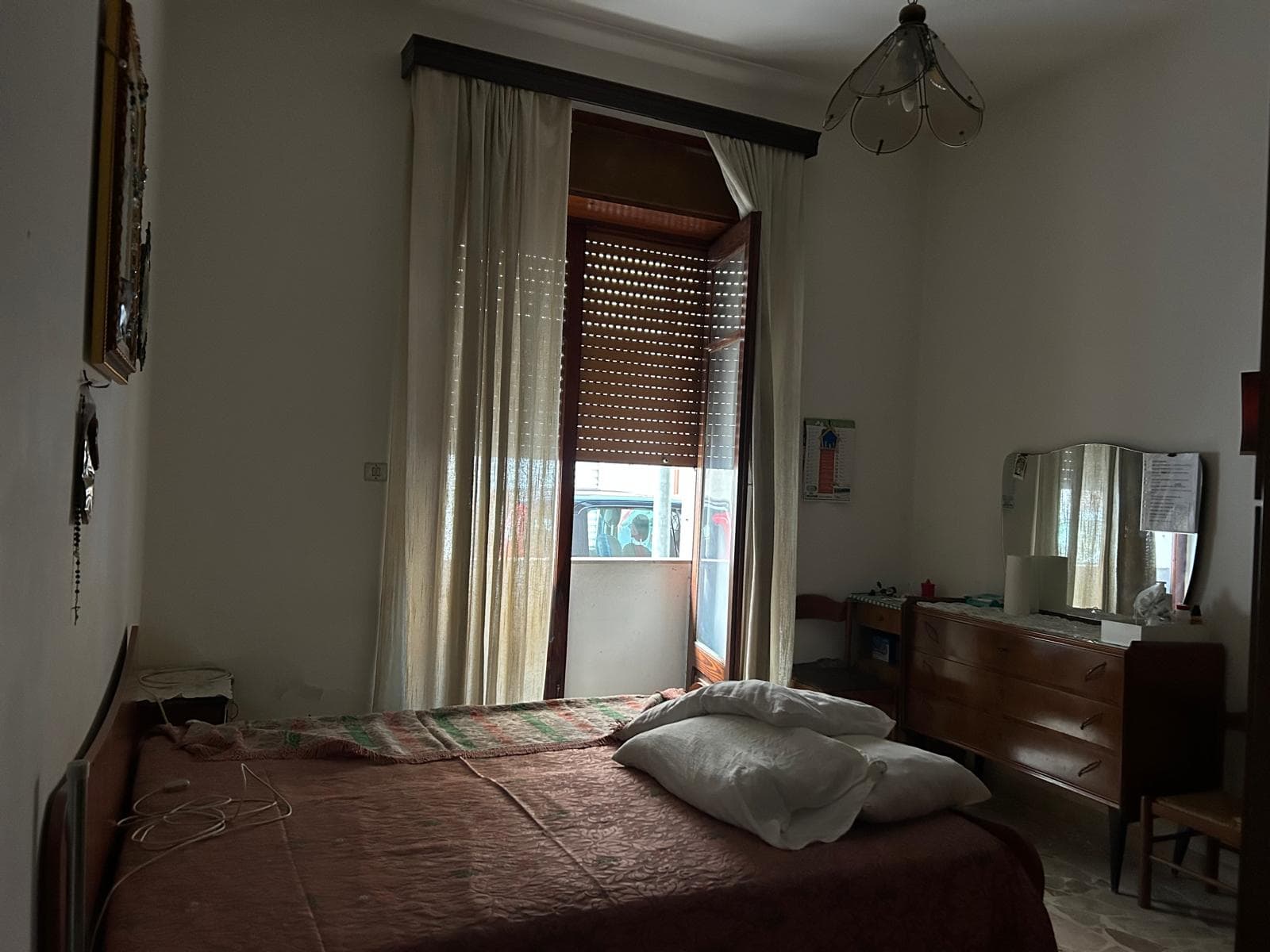 Camera da letto luminosa con finestra grande, tende leggere e arredi in stile classico, ambiente accogliente e tranquillo.