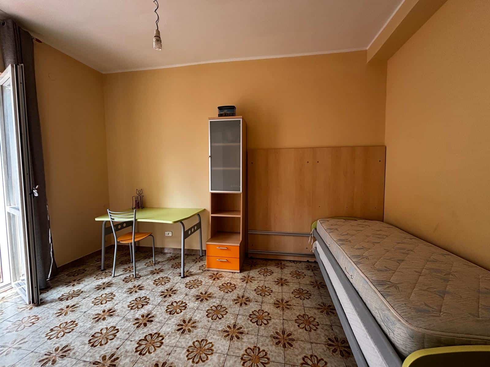Camera da letto semplice con letto singolo, armadio e scrivania, illuminata dalla luce naturale, in un appartamento in affitto a NextCasa.