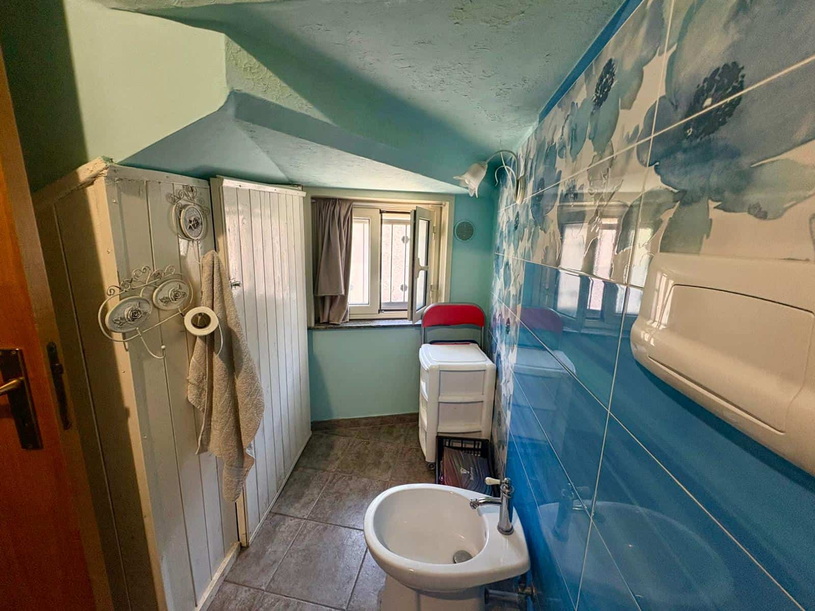 Lavabo e armadietti in bagno con finestra, pareti dipinte di verde e decorazioni murali con nuvole, ambiente luminoso e funzionale, ideale per la ristrutturazione di case e appartamenti.