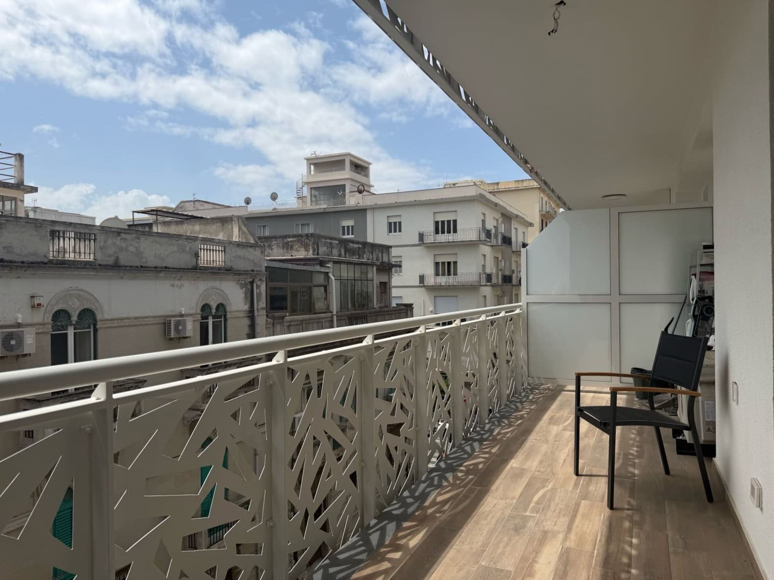 Balcone di un appartamento moderno con ringhiera decorativa, vista su edifici urbani e cielo sereno, ideale per relax e momenti all'aperto in zona residenziale di città.