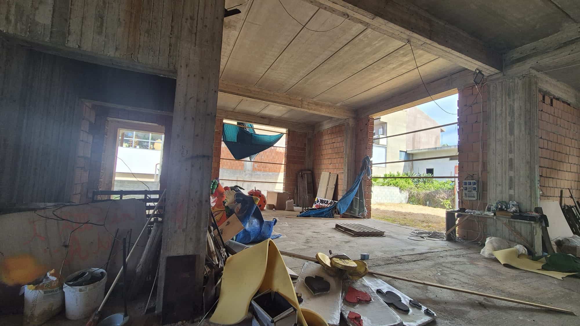 Pannello di costruzione di un edificio residenziale in fase di sviluppo con struttura in cemento e mattoni, attrezzature e materiali da cantiere visibili.