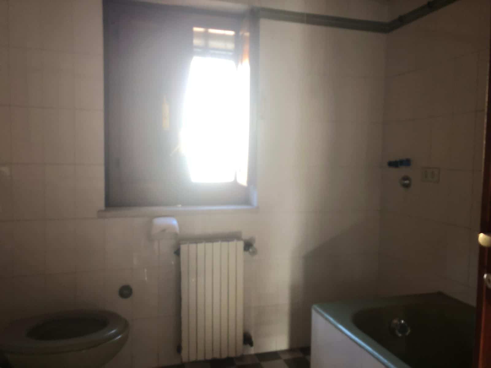 Interno di un bagno con finestra, radiatore e vasca da bagno, ambiente semplice e funzionale, ideale per ristrutturazioni e miglioramenti domestici, NextCasa.