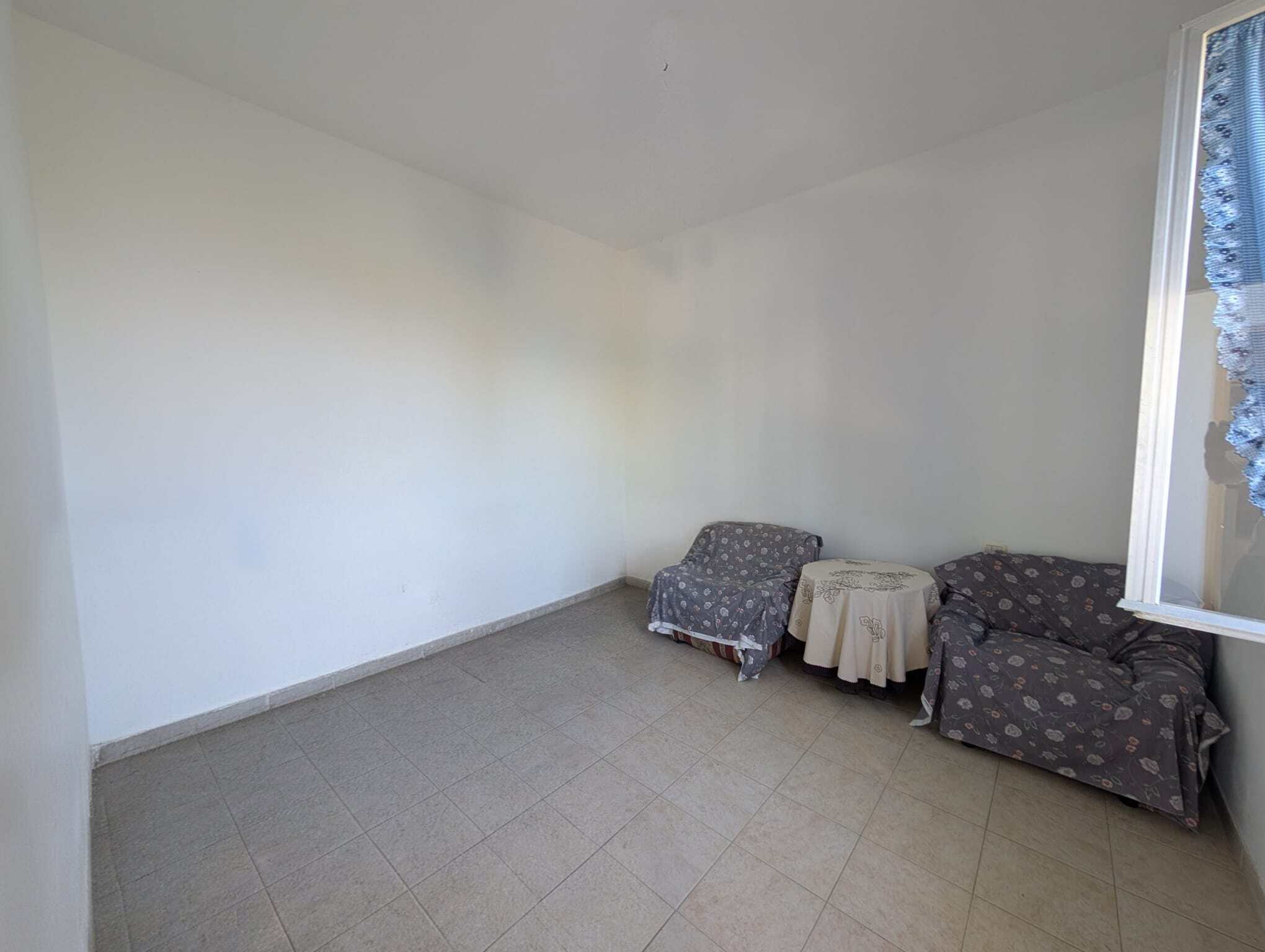 Camera da letto vuota con due poltrone e finestra con tende, ambiente luminoso e semplice, ideale per affitti o ristrutturazioni immobiliari.