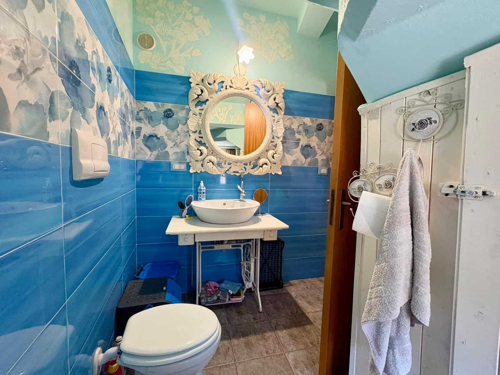 Lavabo e specchio decorativo in un bagno moderno con pareti blu e dettagli eleganti, ideale per ambienti di stile e funzionalità.