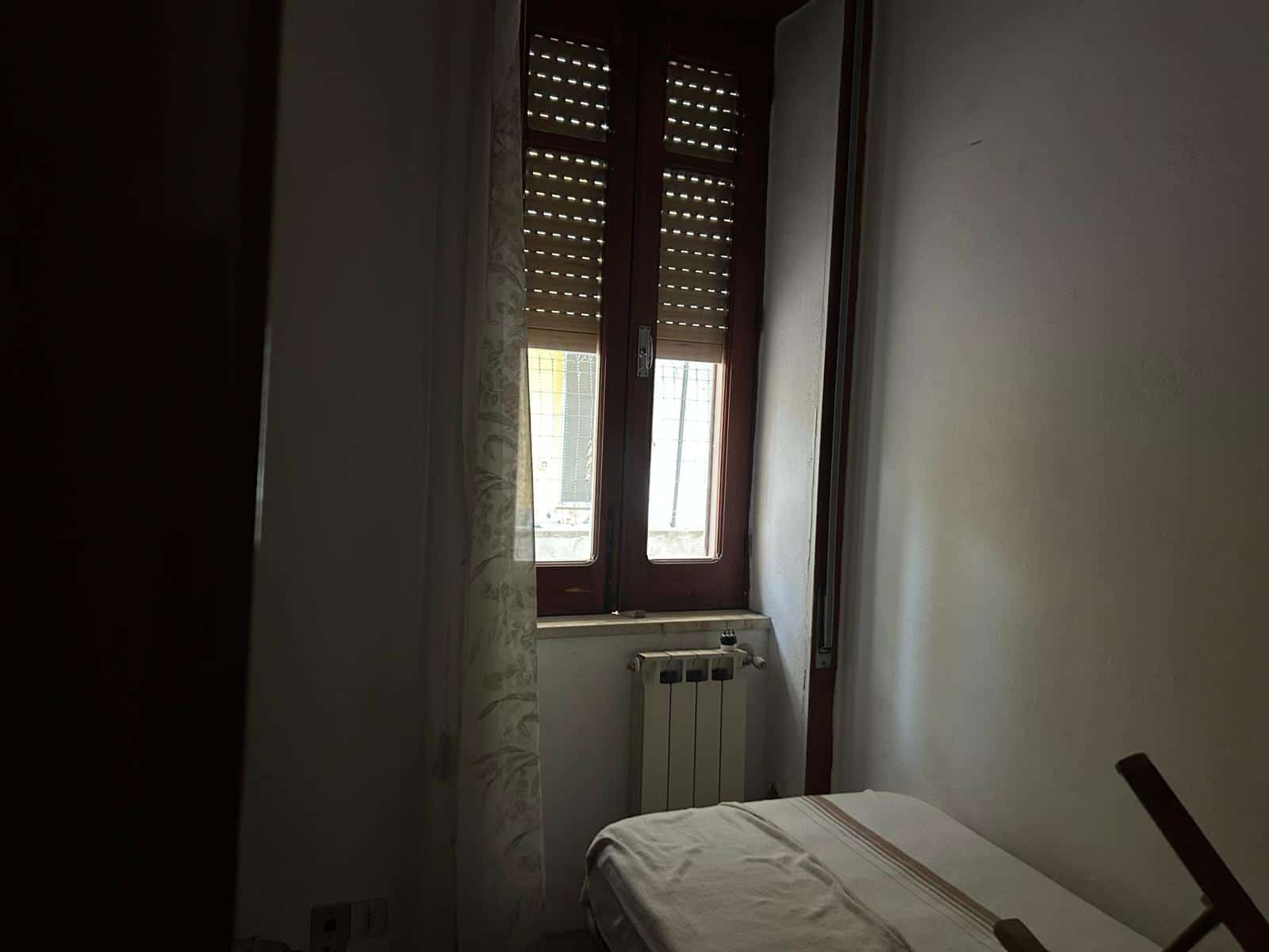 Camera da letto con finestra in legno e tende leggere, ambiente luminoso e semplice, ideale per soggiorni tranquilli.
