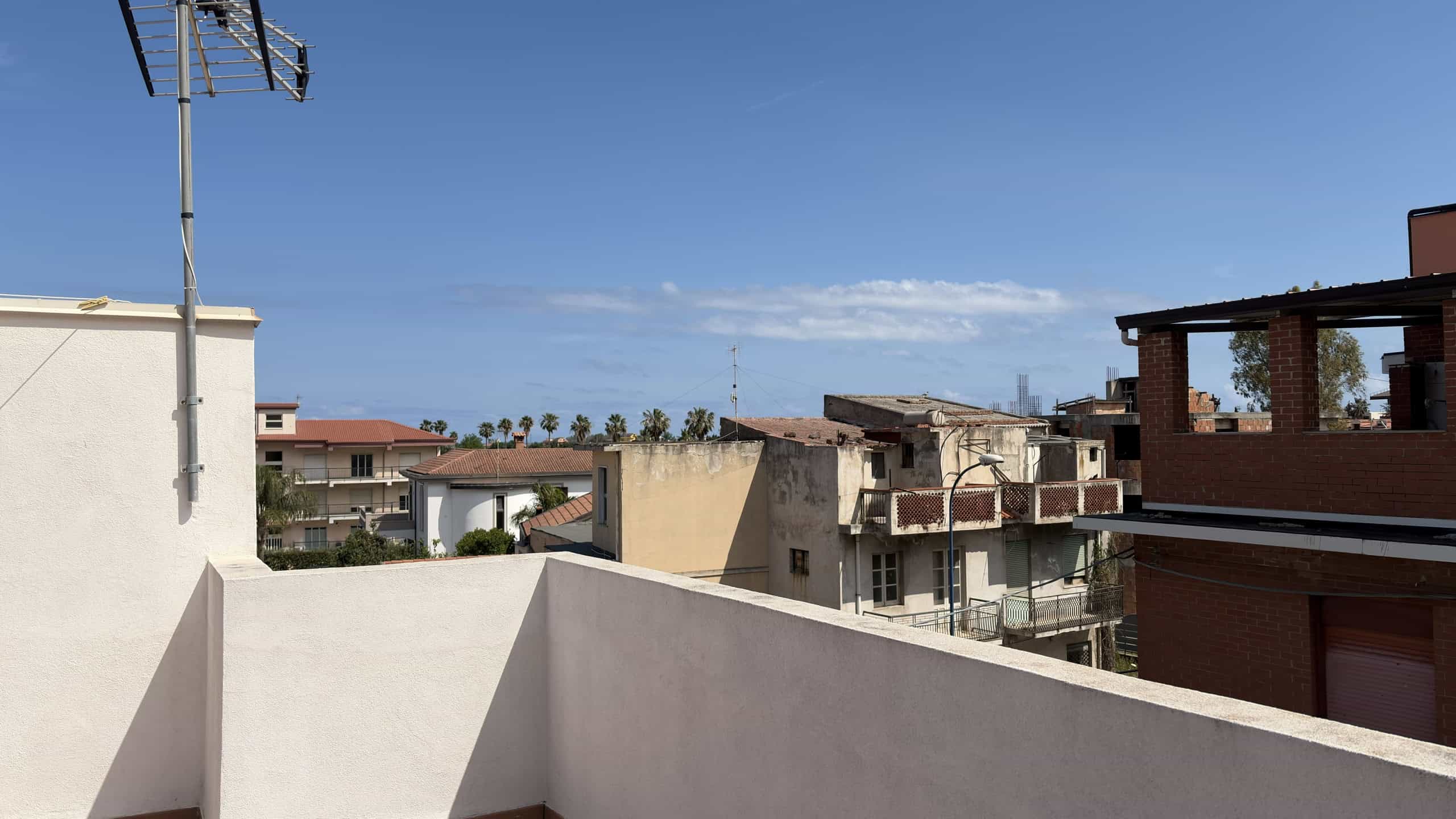 Aggiungi un'antenna TV e un tetto in stile moderno con vista sulla città e sul mare in lontananza, in un ambiente urbano residenziale.