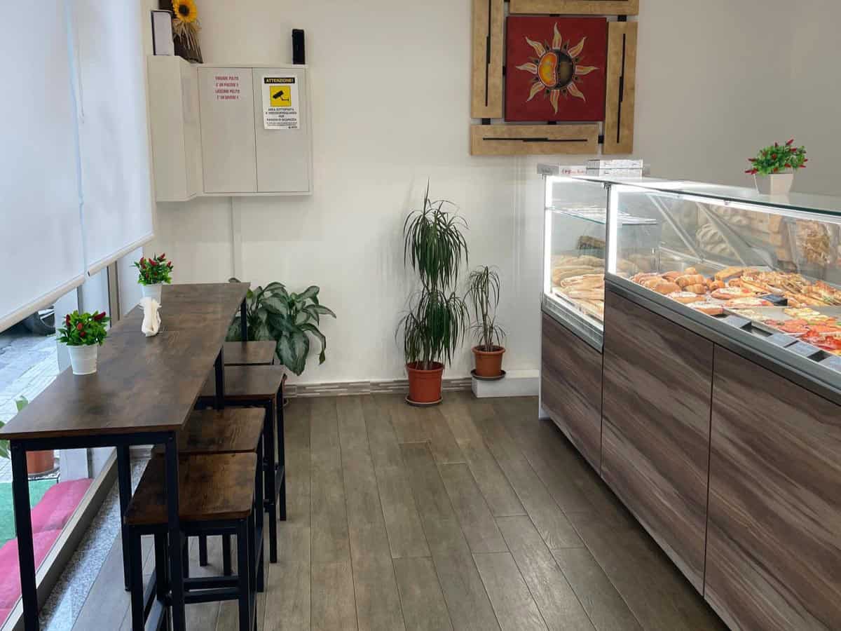 Pannello di esposizione con prodotti da forno in una pasticceria moderna, ambiente accogliente con piante decorative e arredi eleganti, ideale per gustare dolci artigianali e snack.