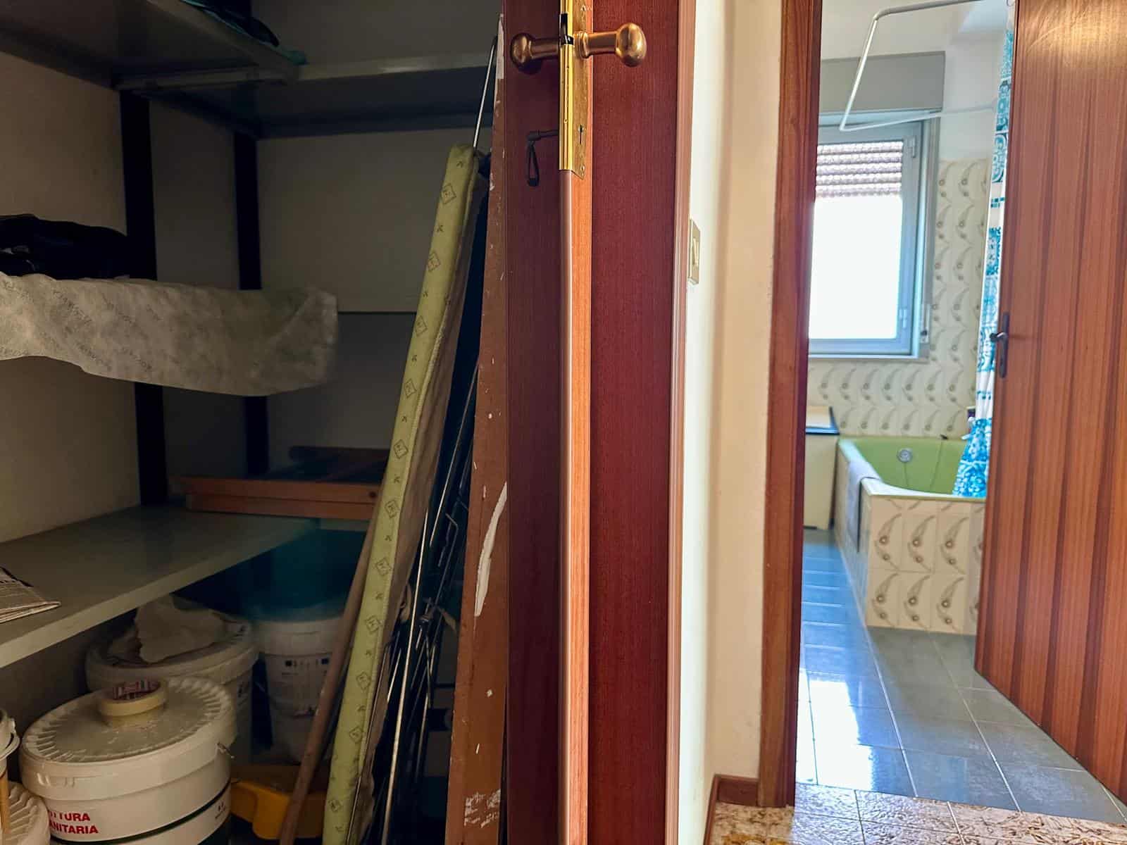 Serratura e porta in legno di una casa, vista dall'interno, con soggiorno e finestra luminosa in background.