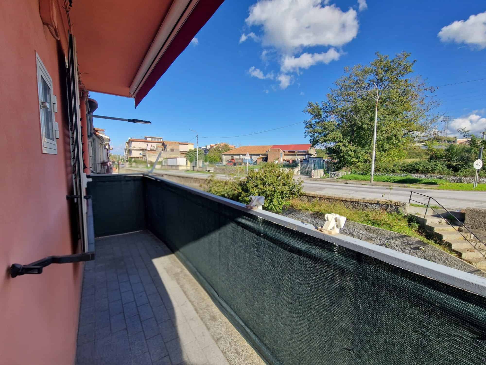 Balcone di un appartamento con vista su strada e natura, cielo sereno, in zona residenziale di NextCasa, Italia.