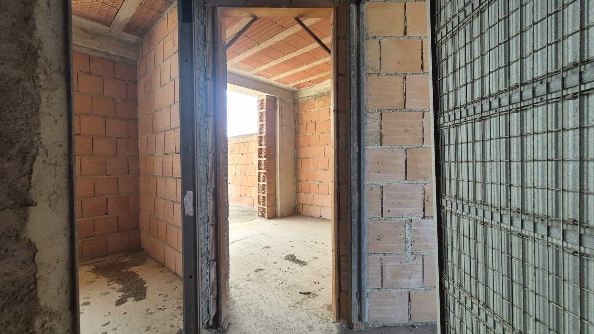 Cantiere edile con pareti in mattoni e struttura in acciaio, pronto per la fase di finitura, con apertura verso l'esterno e illuminazione naturale.