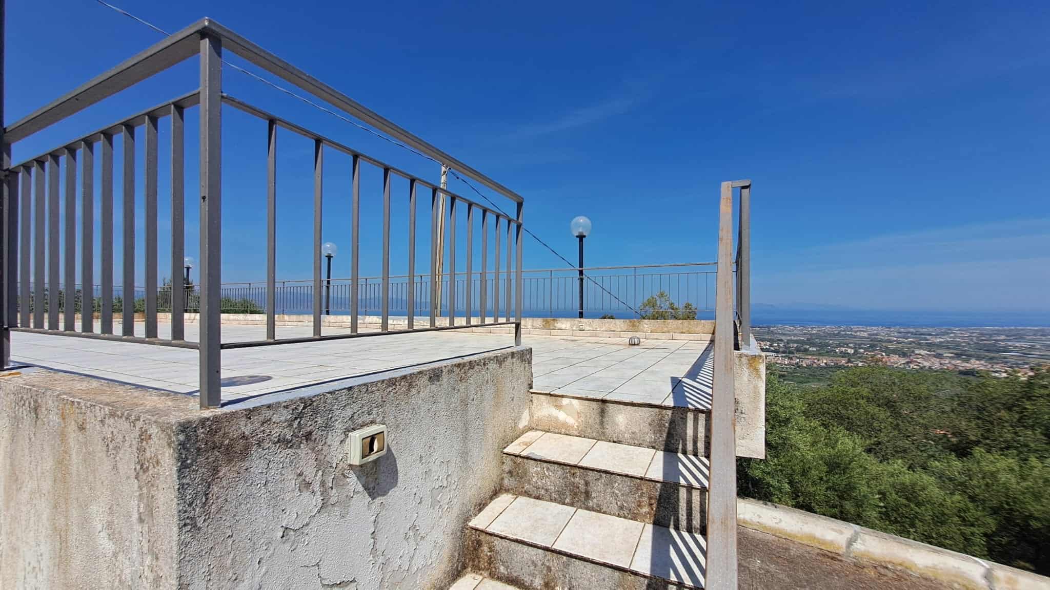 VISTA PANORAMICA dal terrazzo con ringhiera in metallo, che offre una splendida prospettiva sulla città e sulla natura circostante, sotto un cielo azzurro e limpido.