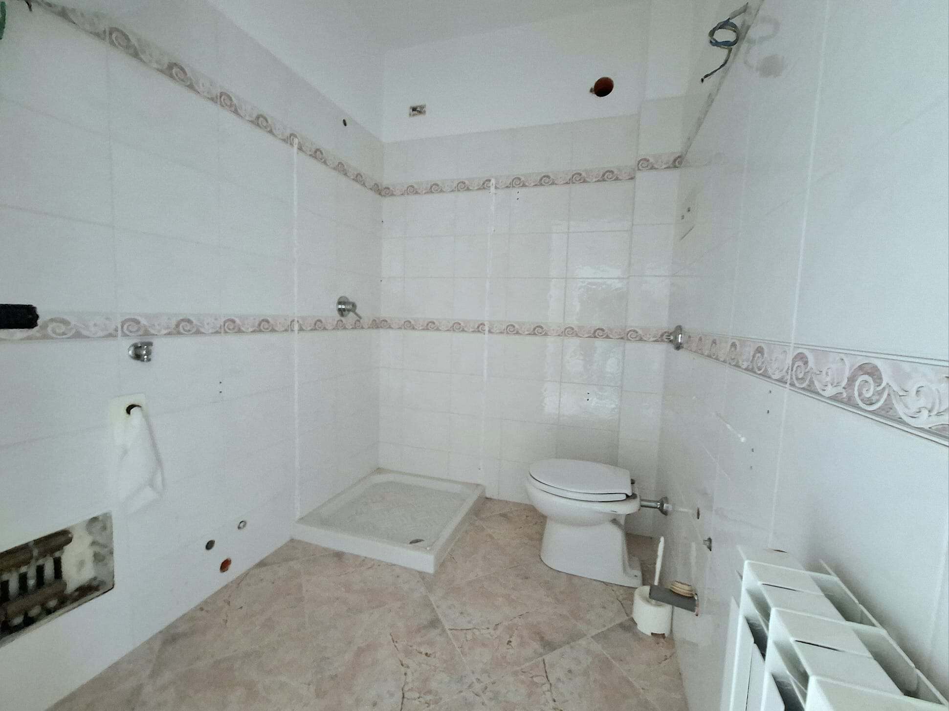 Il bagno in fase di ristrutturazione con pareti rivestite in piastrelle bianche e dettagli decorativi, pronto per essere completato con sanitari e accessori. Ideale per progetti di ristrutturazione di.