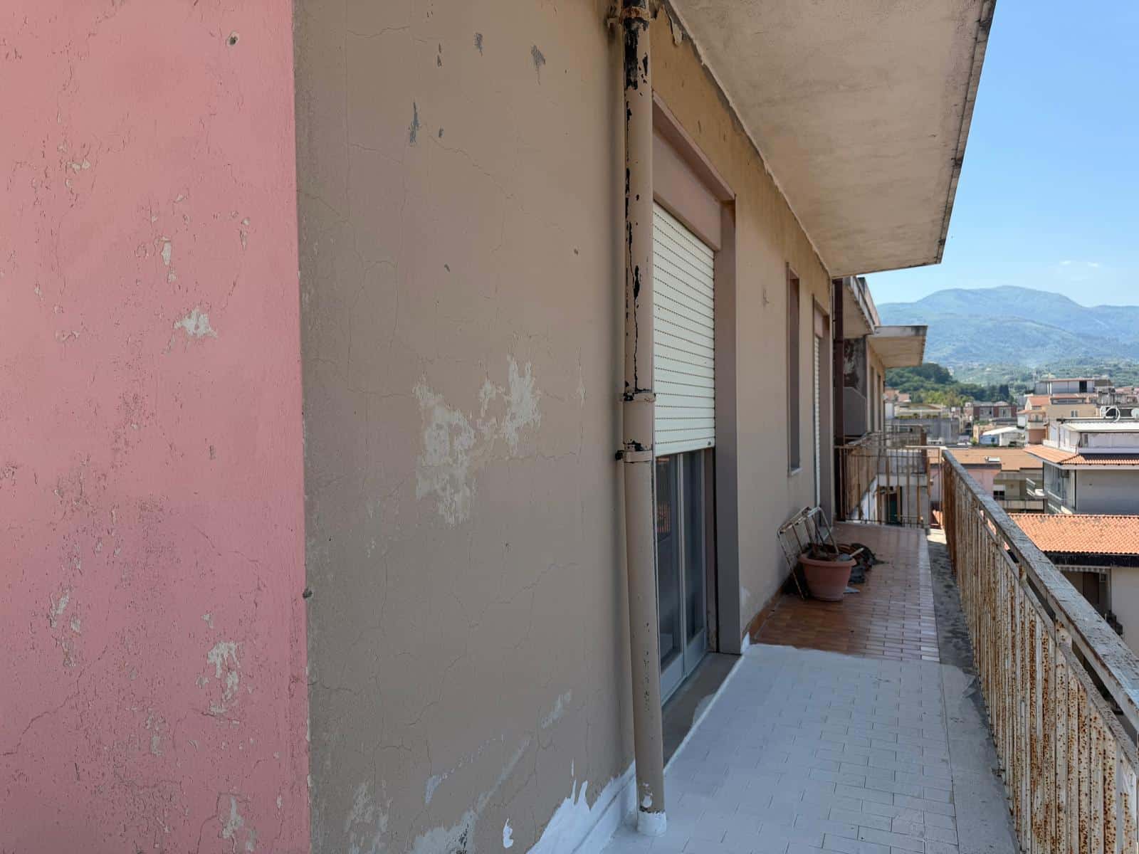 Balcone di un appartamento con vista sulle montagne, pareti esterne con vernice sbiadita e ringhiera in metallo, ambiente urbano e panoramico, ideale per relax e contemplazione.