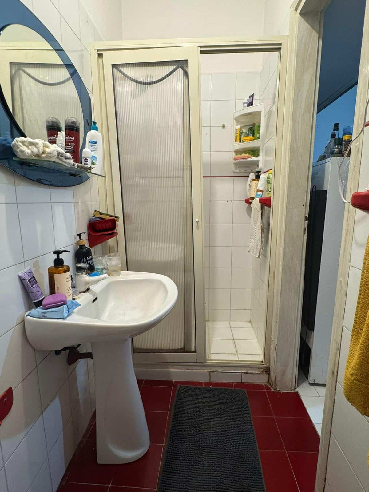 Specchio del bagno con lavabo e doccia, dettagli di arredo e prodotti per la cura personale, in un ambiente domestico funzionale e ben organizzato.
