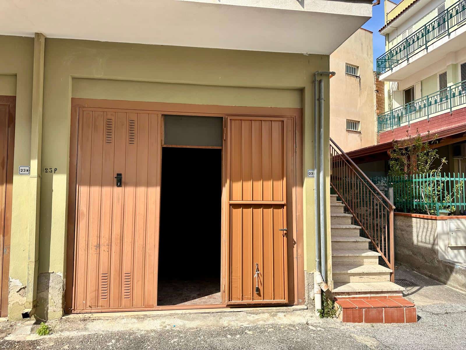 Garage con porta in legno e finestra, situato in edificio residenziale a città, con scale esterne e balconi visibili.