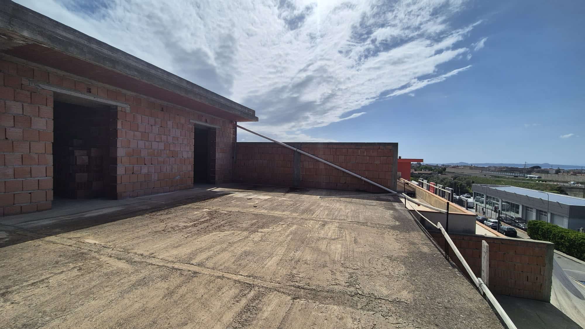 Ampio terrazzo all'aperto con vista panoramica su un edificio in costruzione, cielo sereno e nuvole leggere, ideale per relax e attività all'aperto.