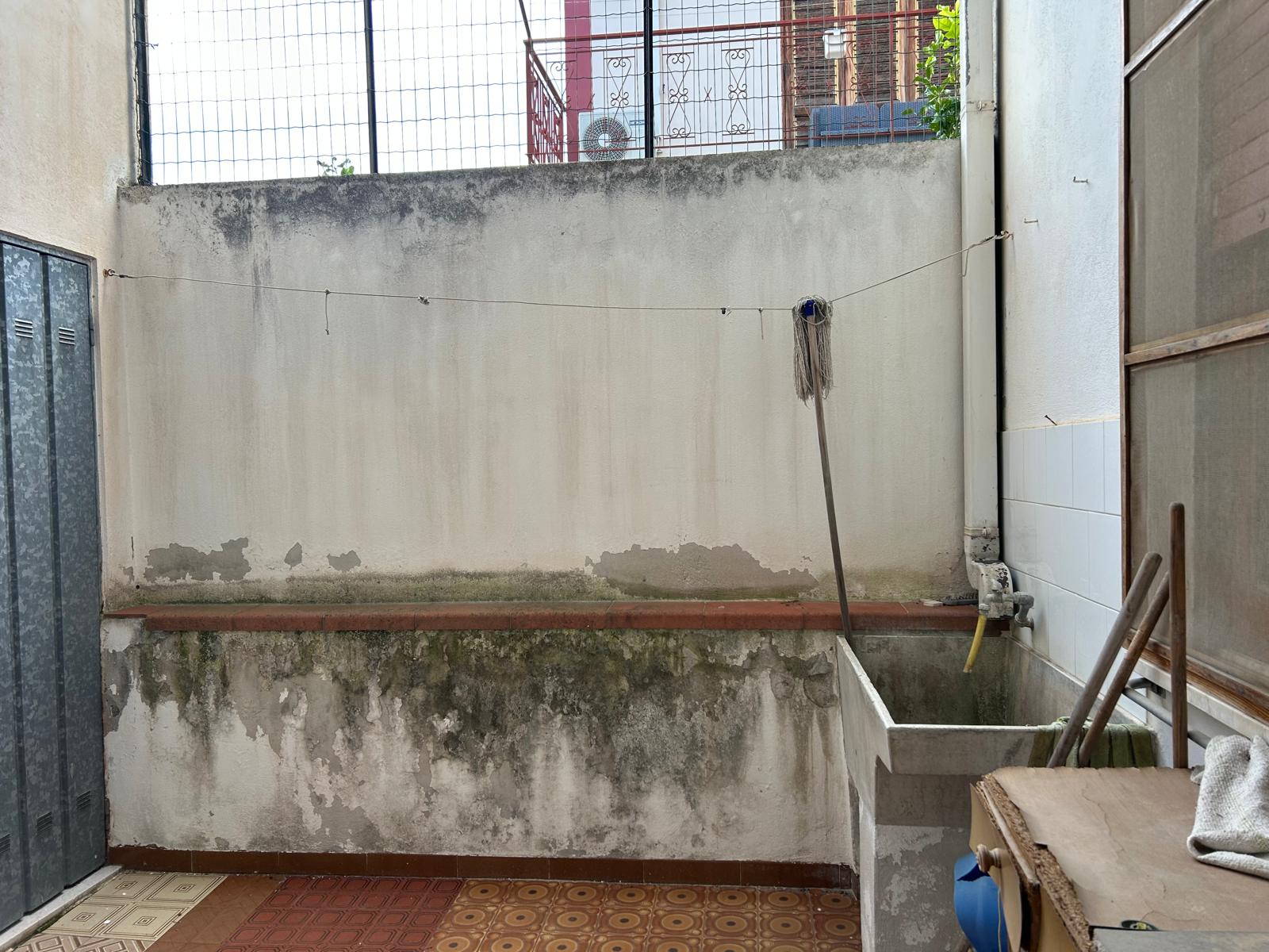 Balcone di un appartamento con pareti macchiate e un lavandino in cemento, ideale per attività di lavanderia o relax all'aperto, in un contesto urbano.