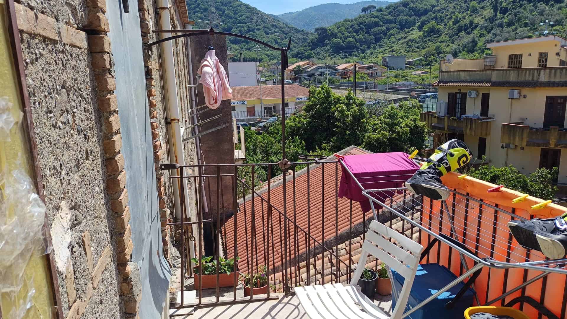 Lavatrice e stendibiancheria su un balcone con vista su case e montagne verdi, in un ambiente residenziale.