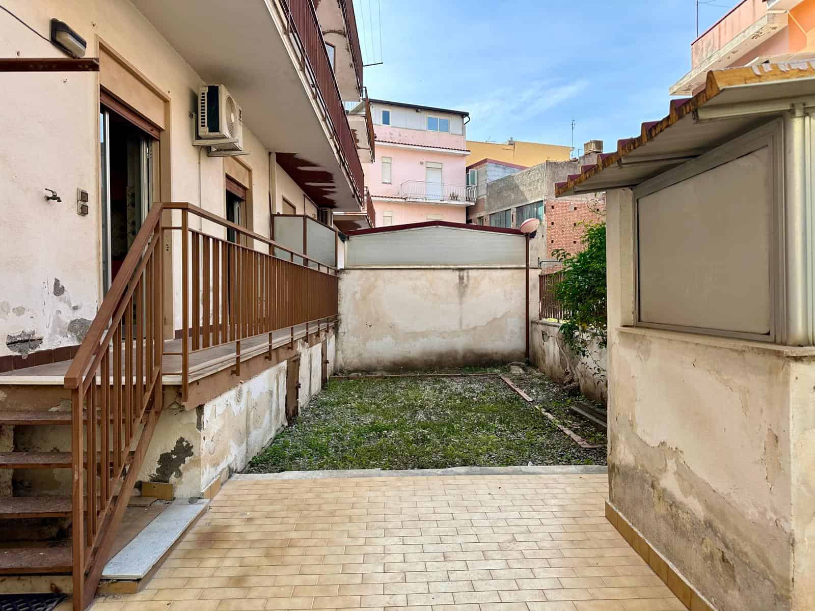 Panchina in legno e spazio esterno con pavimentazione in piastrelle e area verde, ideale per relax e socializzazione in un contesto residenziale urbano.