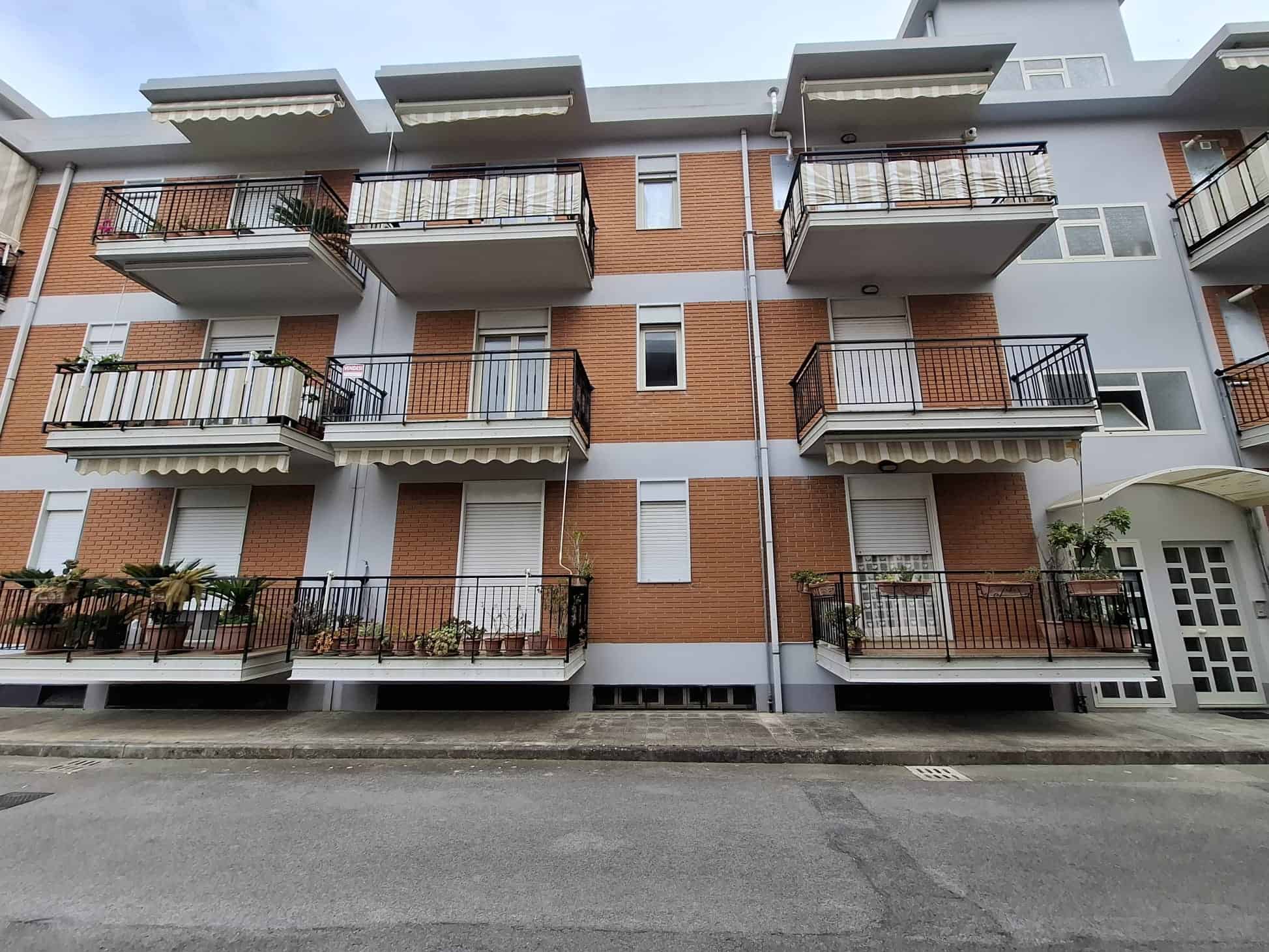 Balcone di un edificio residenziale moderno con ringhiere in metallo e piante ornamentali, facciata in mattoni e dettagli in bianco, in un quartiere urbano.