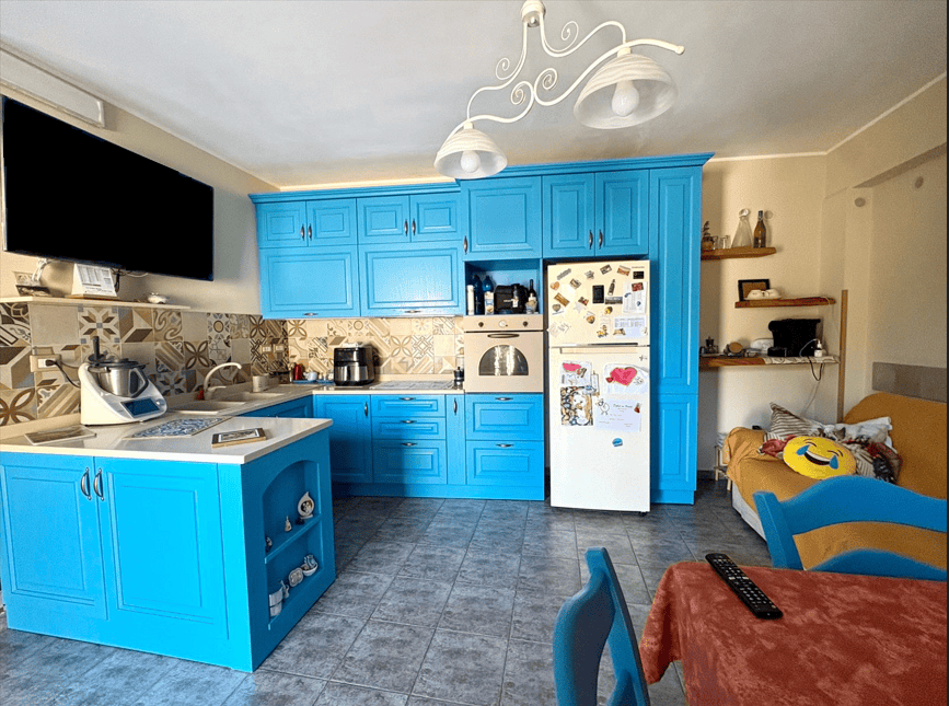 Lavagna di cucina moderna con mobili azzurri, elettrodomestici e dettagli decorativi, ideale per ambienti funzionali e accoglienti. Perfetta per case di design e appartamenti contemporanei.