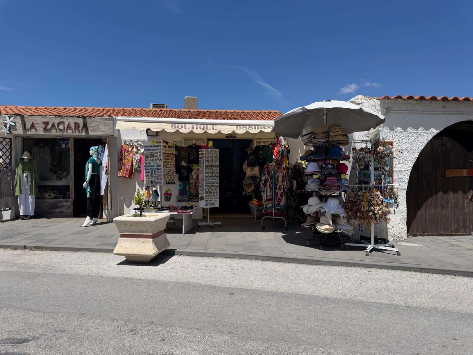 Passeggiata lungo una strada di un villaggio con negozi di souvenir e abbigliamento, negozio di artigianato locale con esposizione di cappelli, accessori e prodotti tipici, cielo sereno e atmosfera es.