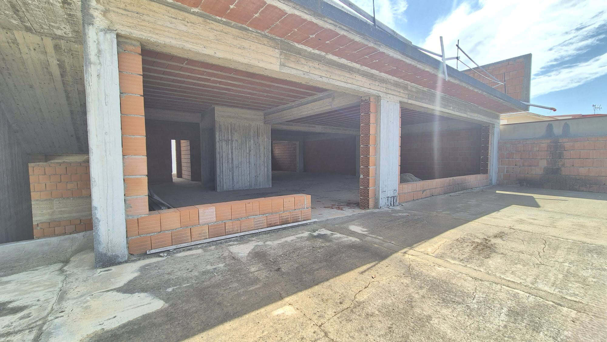 Ampio spazio esterno e struttura in costruzione di un edificio residenziale con pareti in mattoni e cemento, pronto per finiture interne e installazioni.