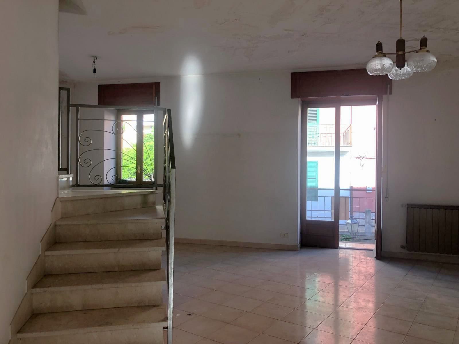 Ampio soggiorno con grandi finestre e porta finestra che permette l'accesso al balcone, illuminato dalla luce naturale, con pavimento in piastrelle e pareti bianche, ideale per vivere e rilassarsi.