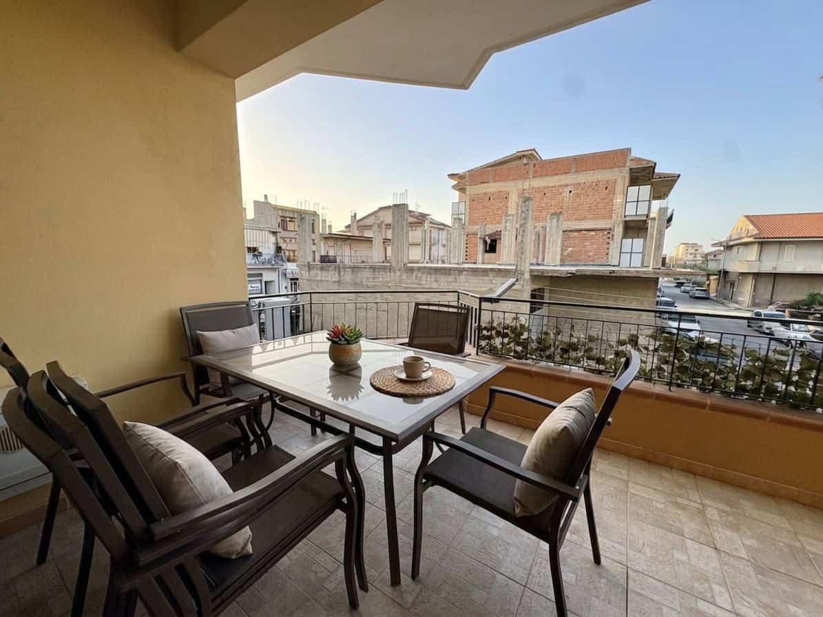 Balcone di un appartamento con tavolo e sedie, vista su edifici residenziali in un quartiere urbano, luce naturale, atmosfera accogliente e moderna.