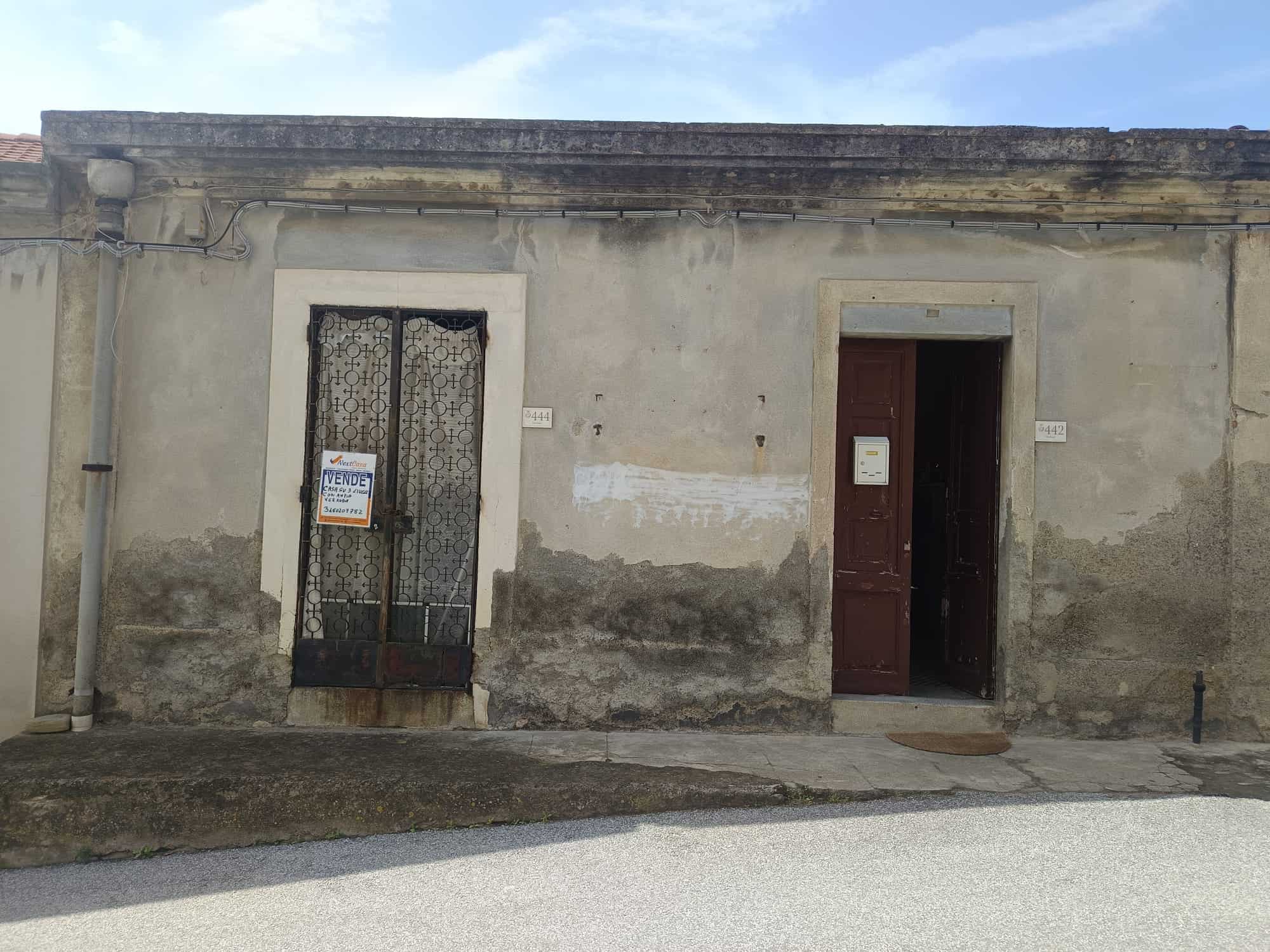 Porta d'ingresso e finestra di una casa antica con pareti in pietra e intonaco, in un contesto urbano italiano.