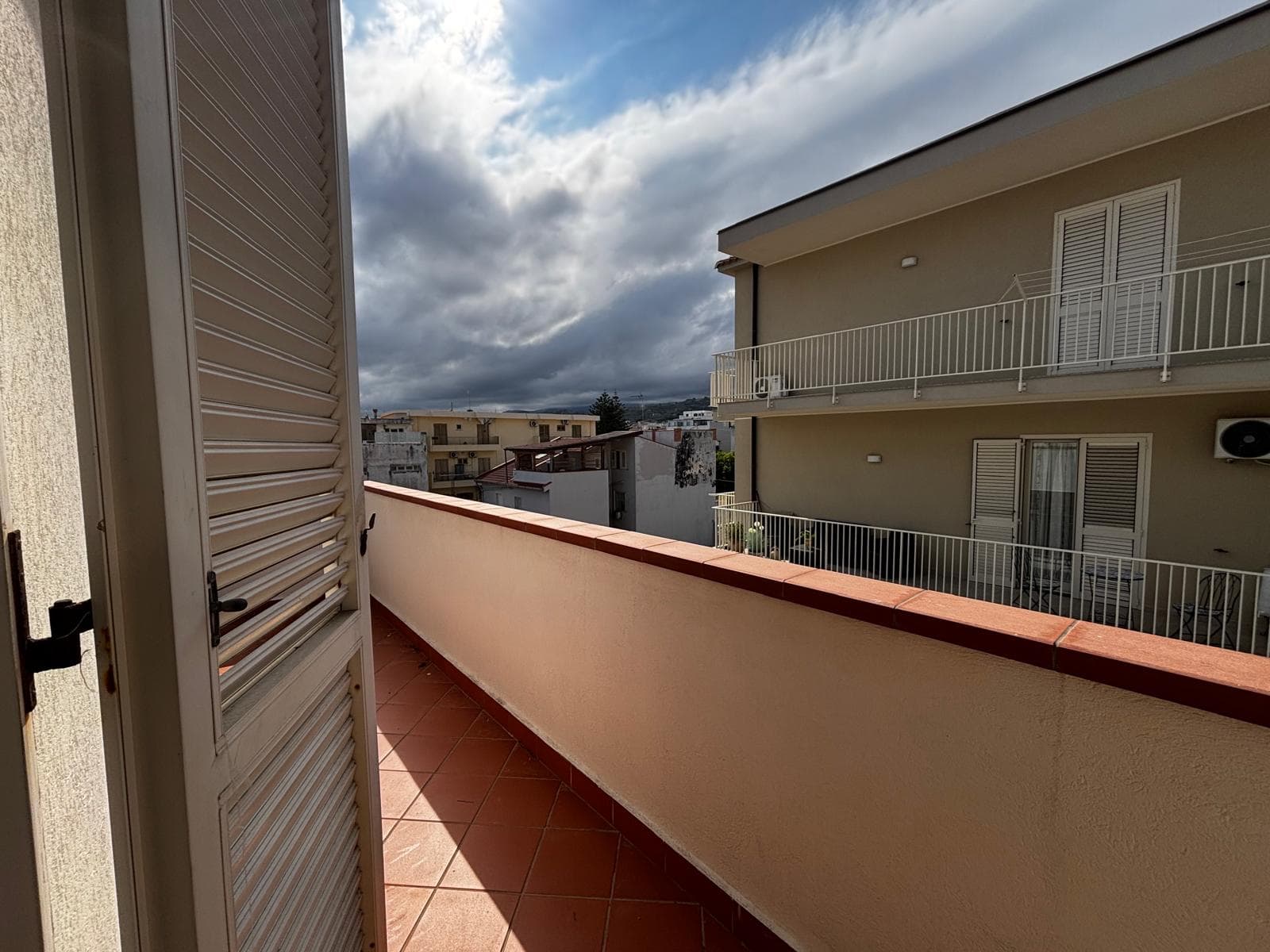 Ampia terrazza soleggiata con vista su edifici residenziali e cielo nuvoloso, ideale per relax e momenti all'aperto.