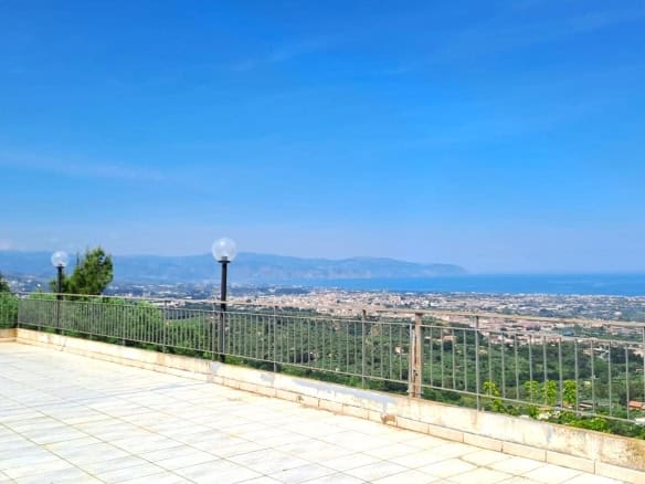 Vista panoramica sulla città e sul mare dal terrazzo di una casa con pavimentazione in piastrelle e lampioni decorativi, immersa nel verde e con un ampio orizzonte.