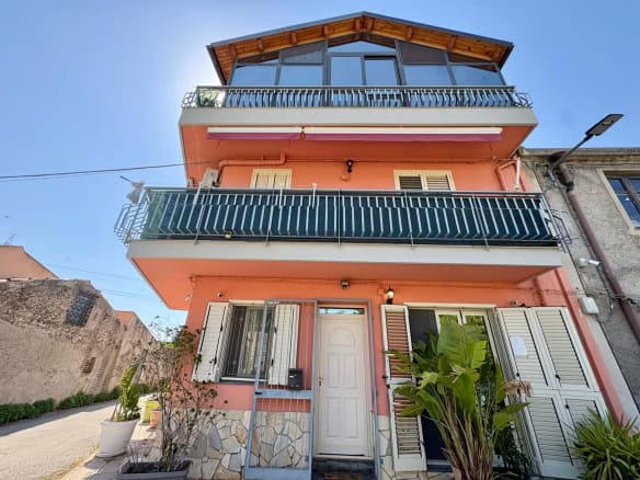 Casa moderna a tre piani con balconi e terrazza panoramica, facciata rosa e dettagli in pietra, situata in zona residenziale soleggiata.