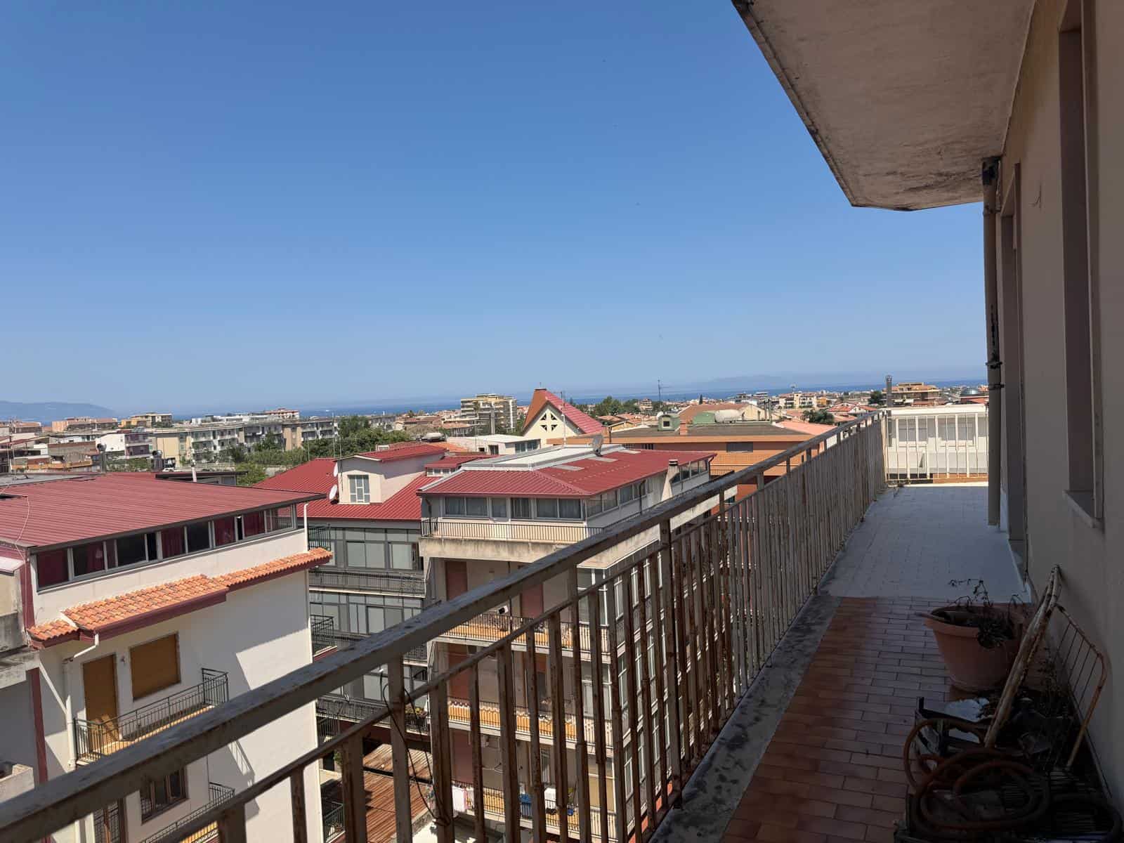 Balcone di un appartamento con vista panoramica sulla città e sul mare, in un giorno soleggiato. L'immagine mostra un balcone con pavimentazione in piastrelle e ringhiera in metallo, ideale per relax.
