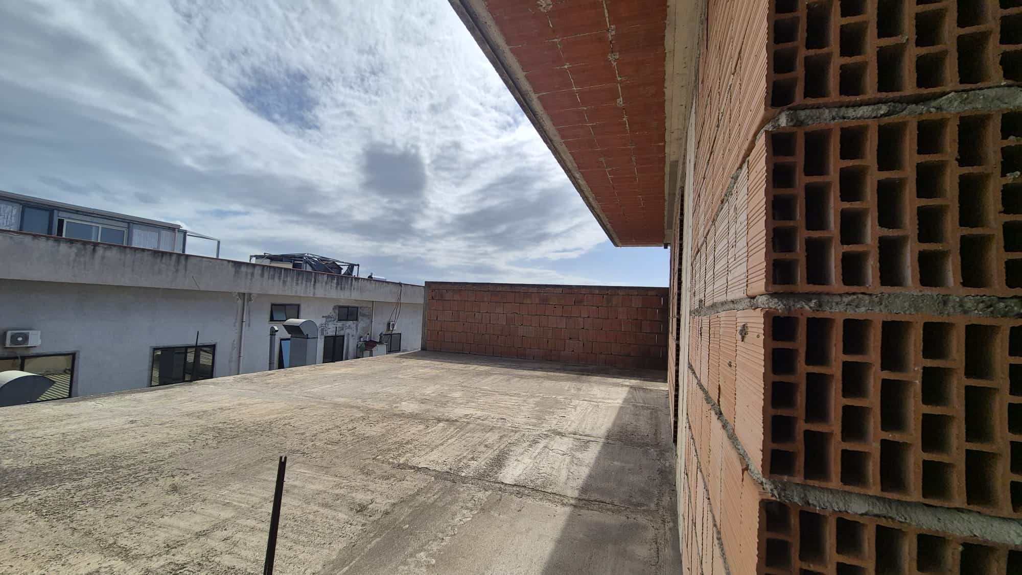 Balcone di un edificio in fase di costruzione con vista sul cielo nuvoloso, pareti in mattoni e superficie in cemento, pronto per lavori di finitura e installazioni future.