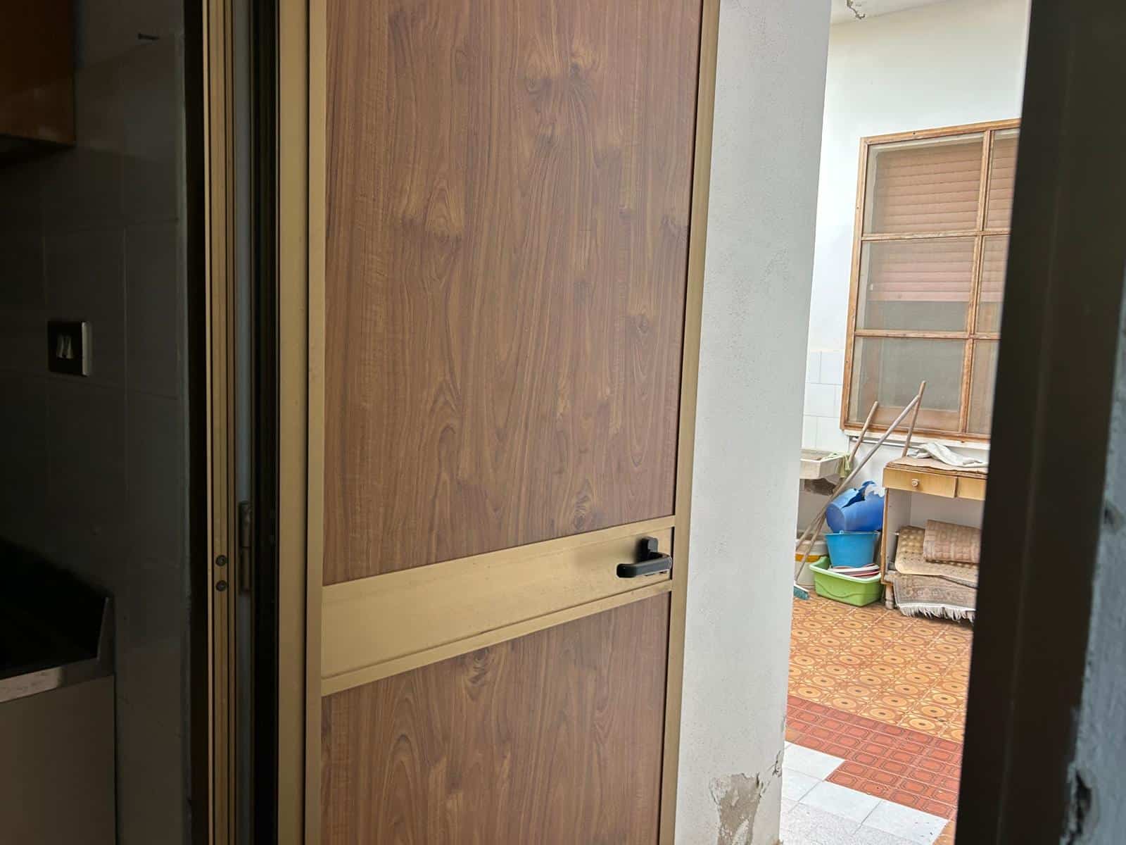 Il portone d'ingresso in legno con maniglia nera, vista dall'interno di un appartamento, con un'area esterna e mobili in background, ideale per immagini di ristrutturazioni o design di interni.