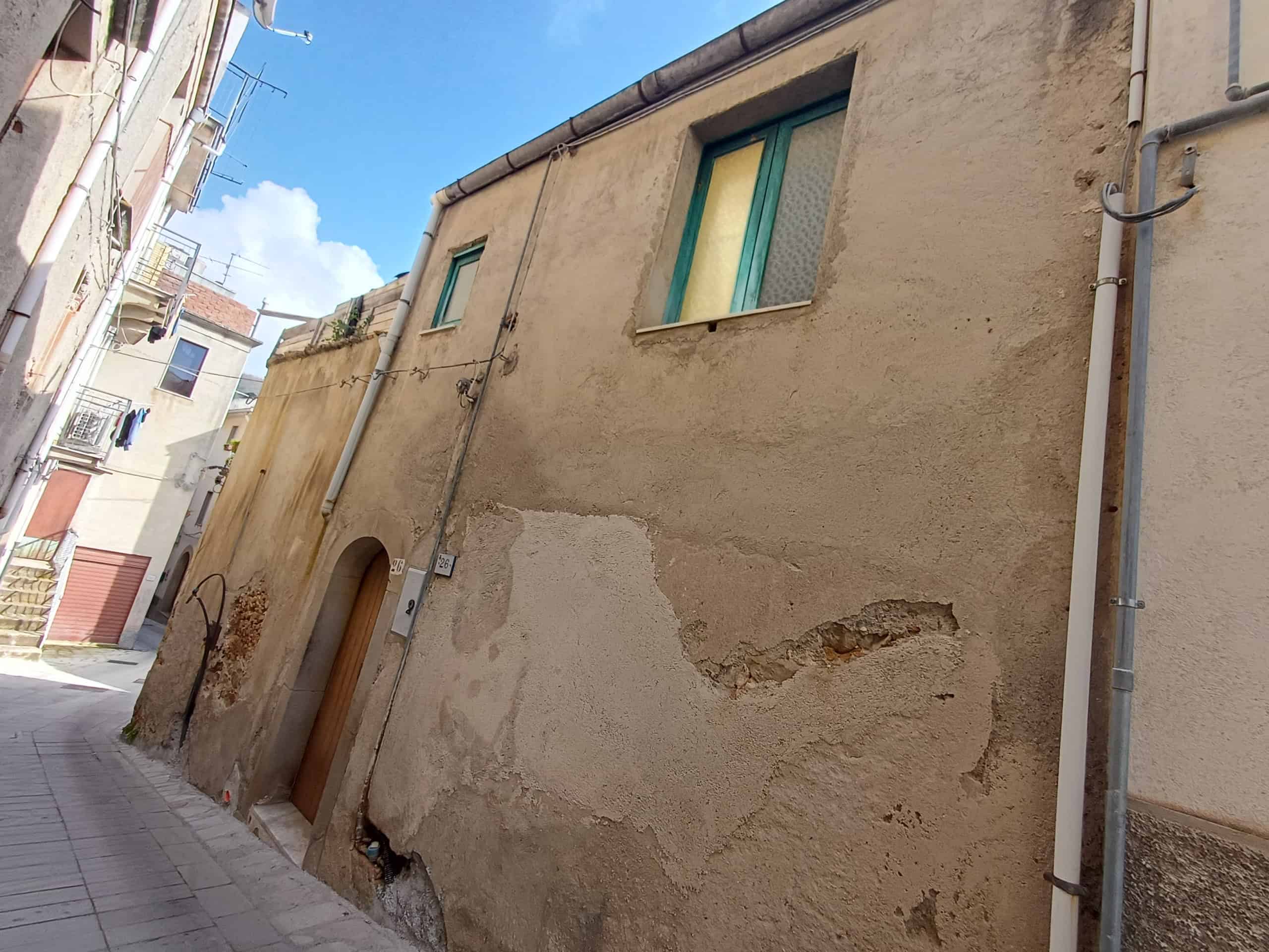 Vernice e muratura di un edificio storico in centro città, con pareti in pietra e intonaco deteriorato, situato in una strada urbana stretta.