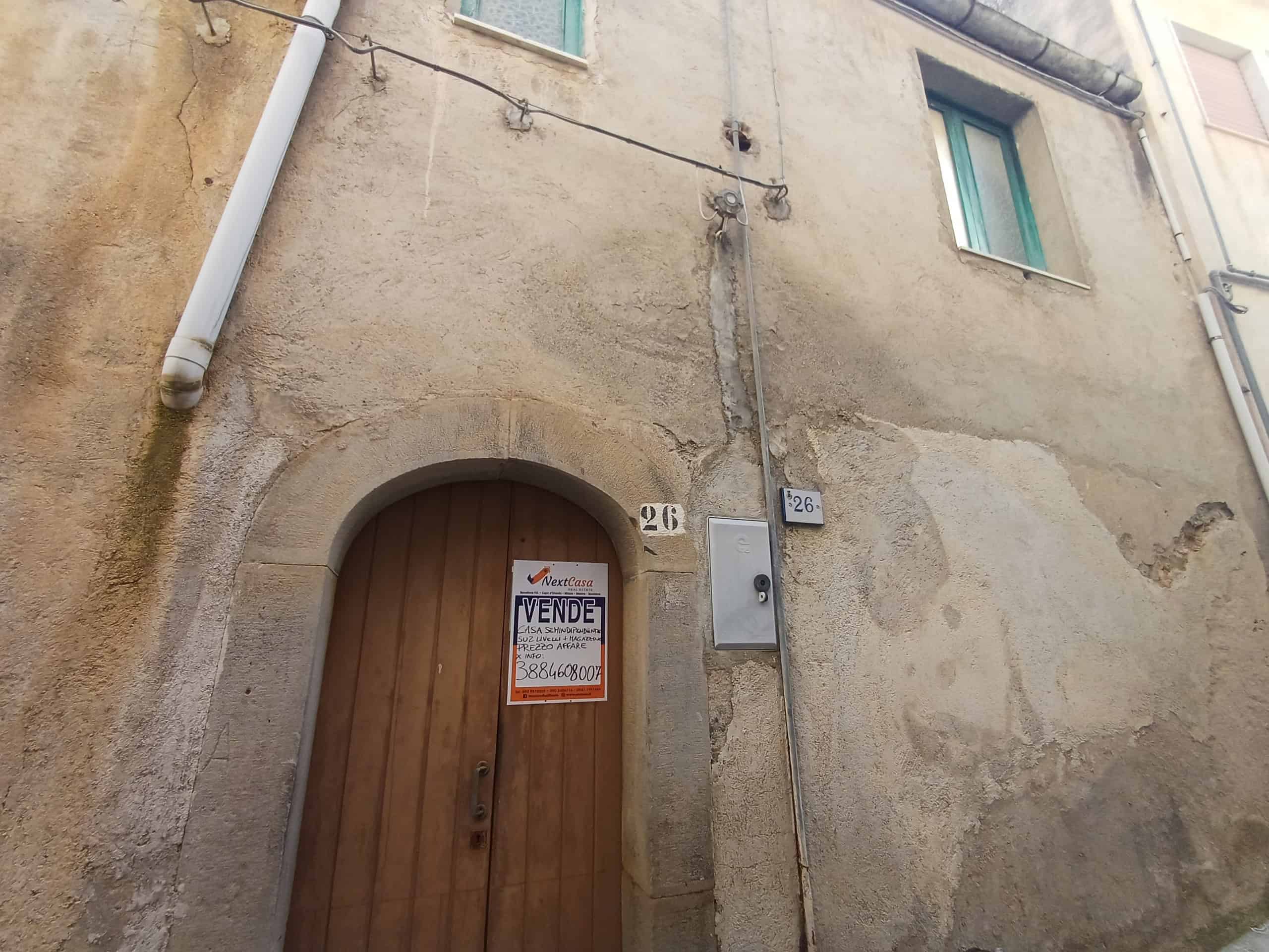 Casa storica in vendita con porta in legno e pareti in pietra, situata in zona urbana.