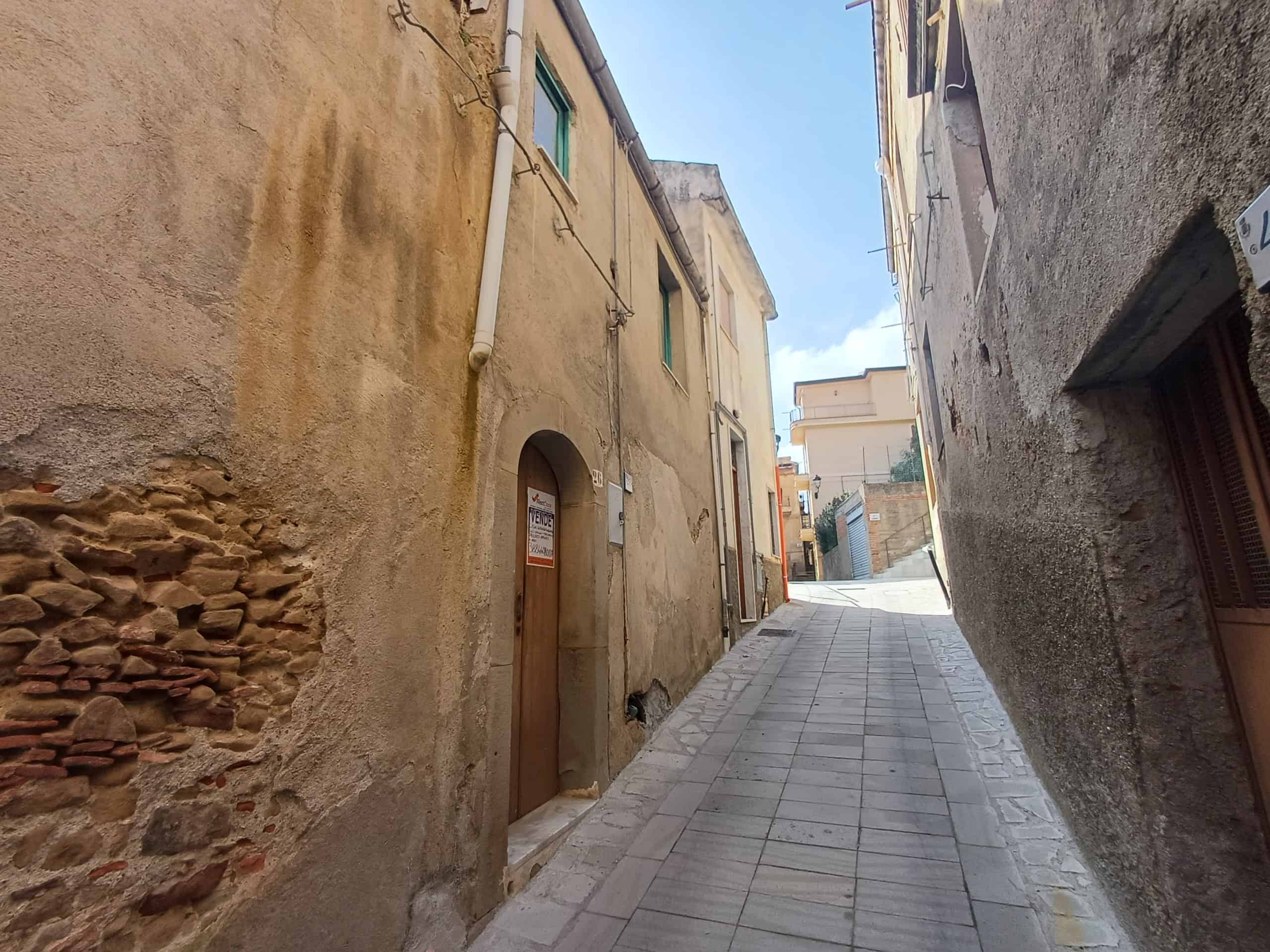 Vicolo stretto e suggestivo di Napoli con case antiche e pavimentazione in pietra, in pendenza, che mostra l'atmosfera autentica e il fascino del centro storico napoletano.