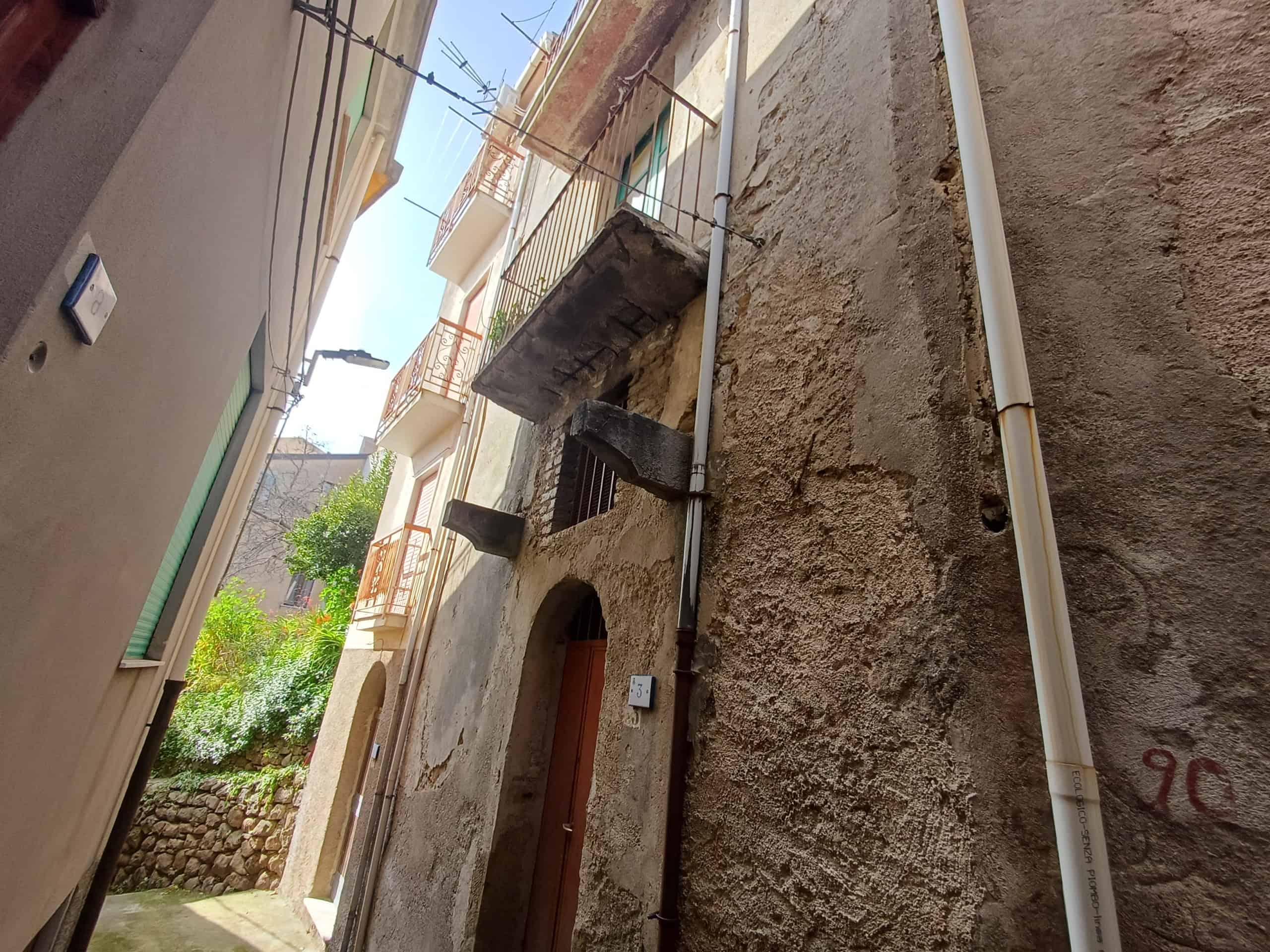 Vicolo stretto tra edifici storici con pareti in pietra e balconi in ferro battuto, in un quartiere tradizionale italiano.