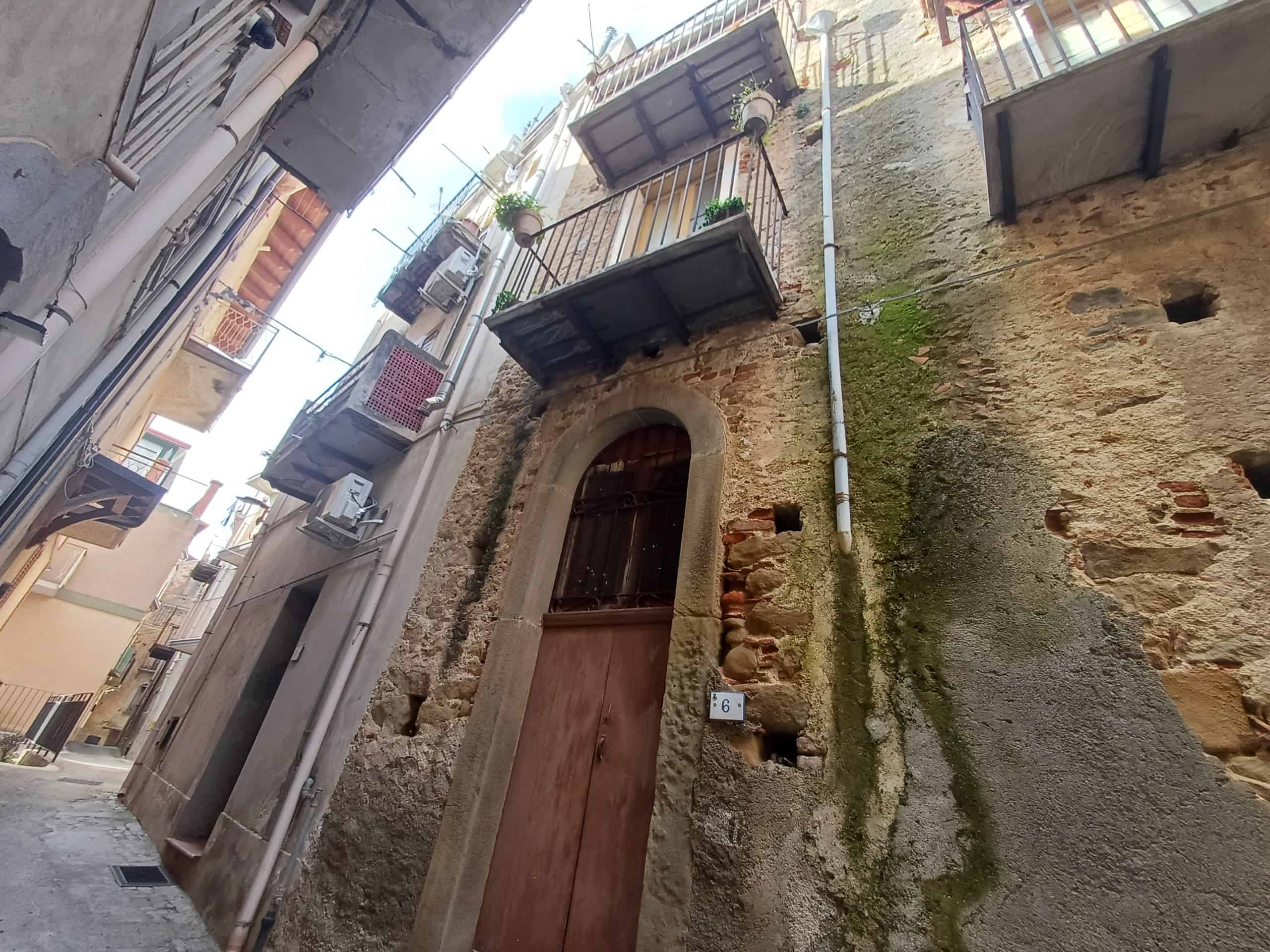 Casa storica con balconi e pareti in pietra, in un vicolo di città.